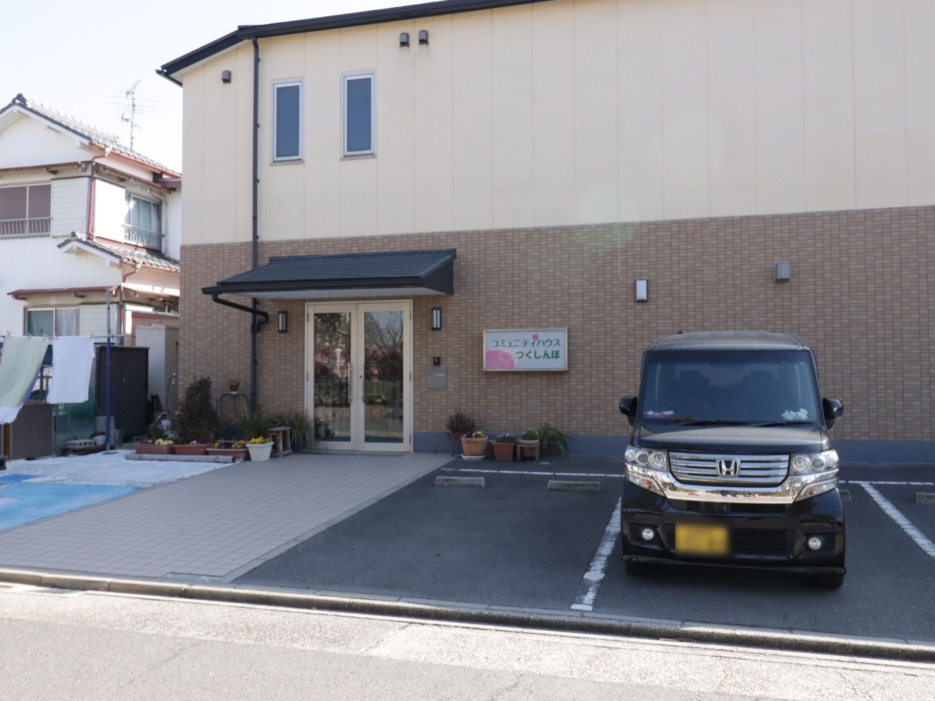 施設入口の横には施設名称のプレートが貼られており、駐車場が完備されている。道路から施設入口まで歩行路のスペースが設置されている。