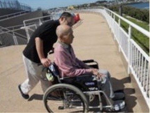 車椅子ご利用の男性の方の外出にサポートしている男性スタッフ