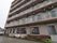 6階建てのマンションのような建物である。2階以上には隣室とつながったベランダが続いている。エアコンの室外機がひさしに吊されている。