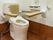 外付けの手すりが付いた洋式トイレがあり、その前に跳ね上げ式の手すりが下りている。手すりが設置してある壁にはナースコールも取り付けられている。