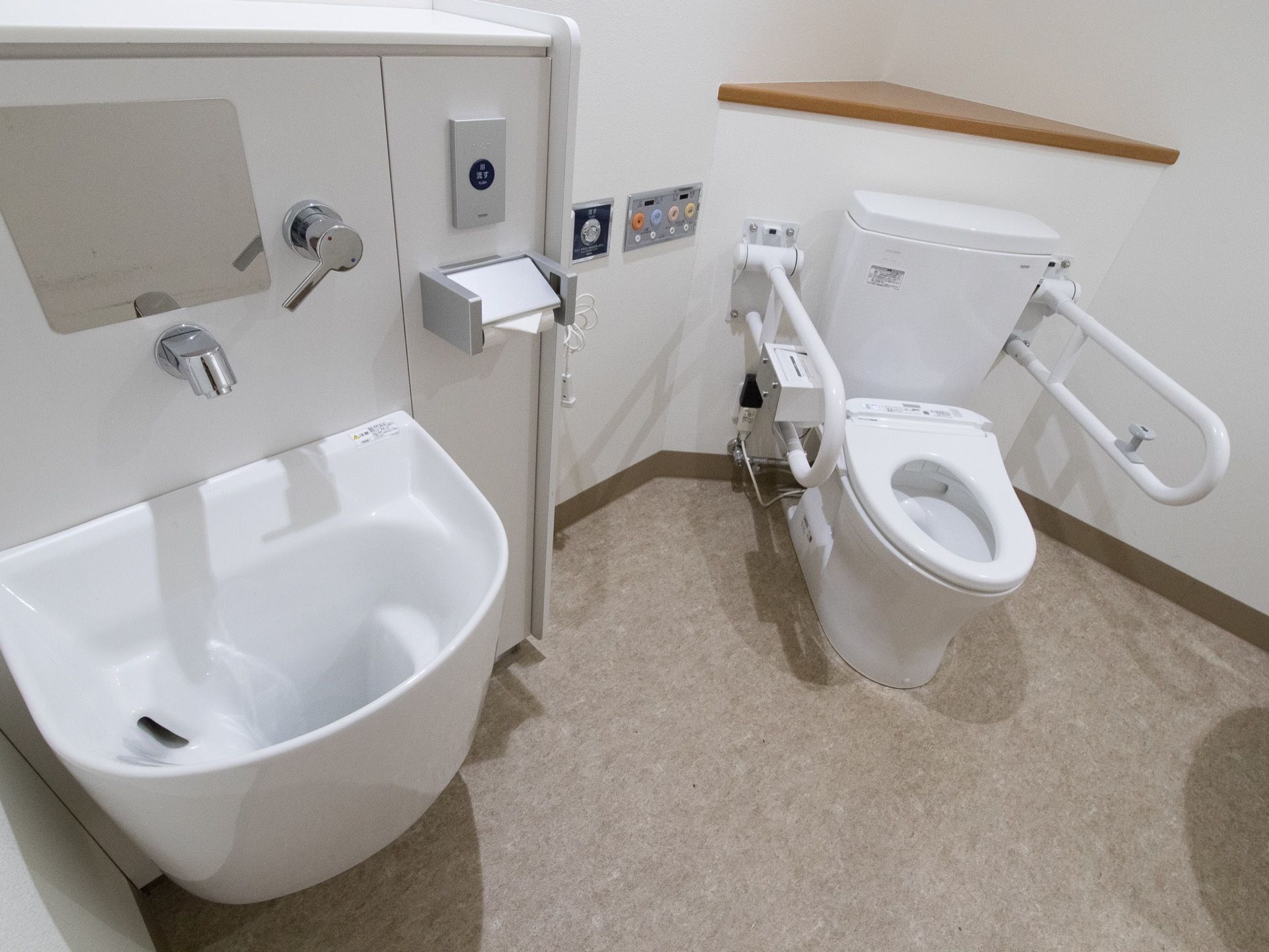 手すりがトイレの脇に設置されている。暖房便座付き温水洗浄トイレがある。呼び出しボタンがある。汚物流しが隣にある。