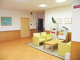 広い玄関ホールの一角に、黄色のソファと木目調のテーブルが置かれている。側にはラックがあり、雑誌類が用意されている。