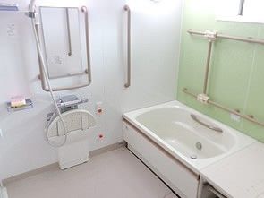 明るく清潔感のある浴室である。浴槽の中にはステンレス製の手すりが付いている。浴槽の向こう側には入浴を助けるリフターがある。