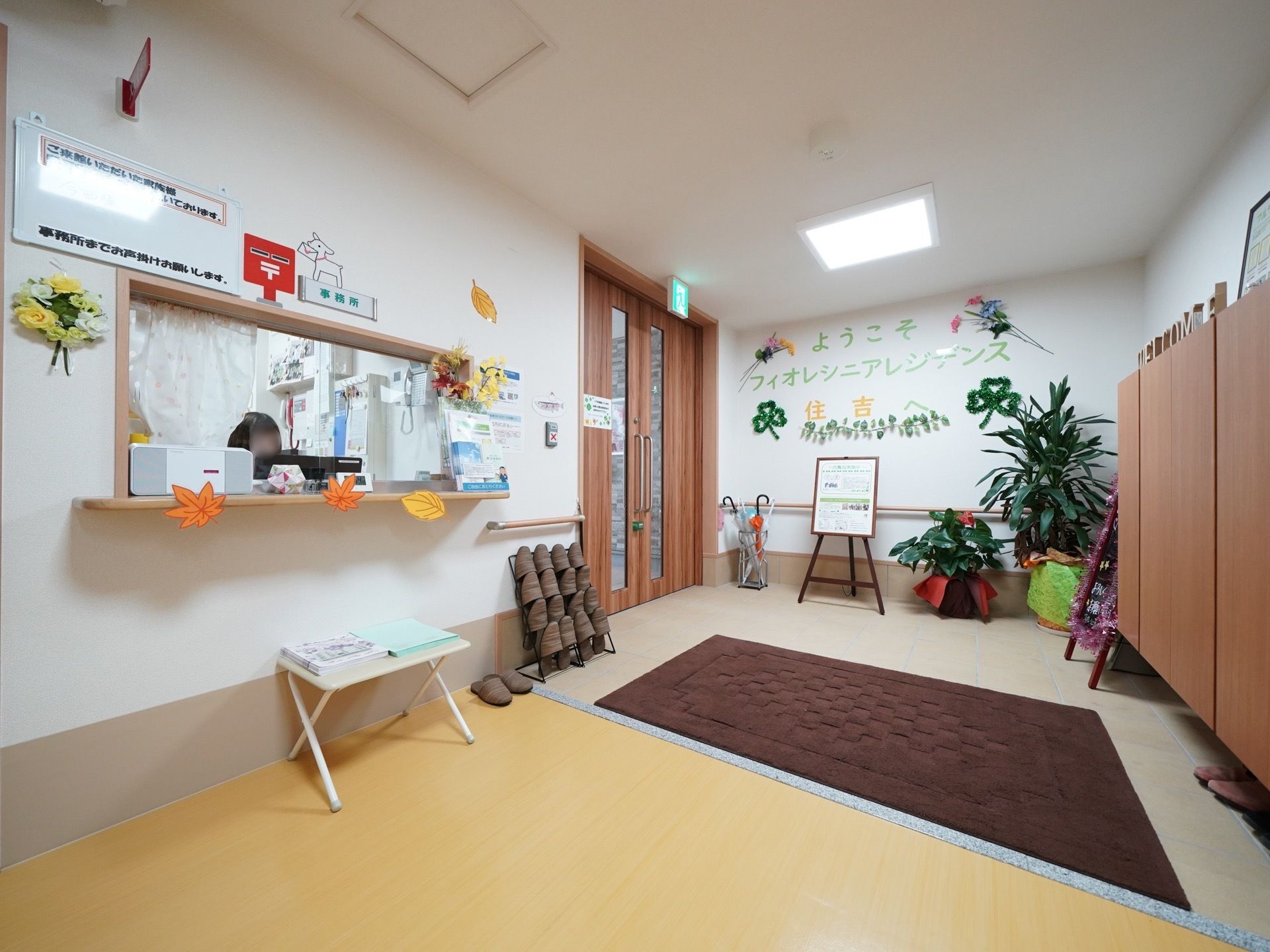 ドアを開くと広い玄関フロアになっている。正面に大きな靴箱があり、壁際に傘立て、観葉植物、ウェルカムボードが置かれている。