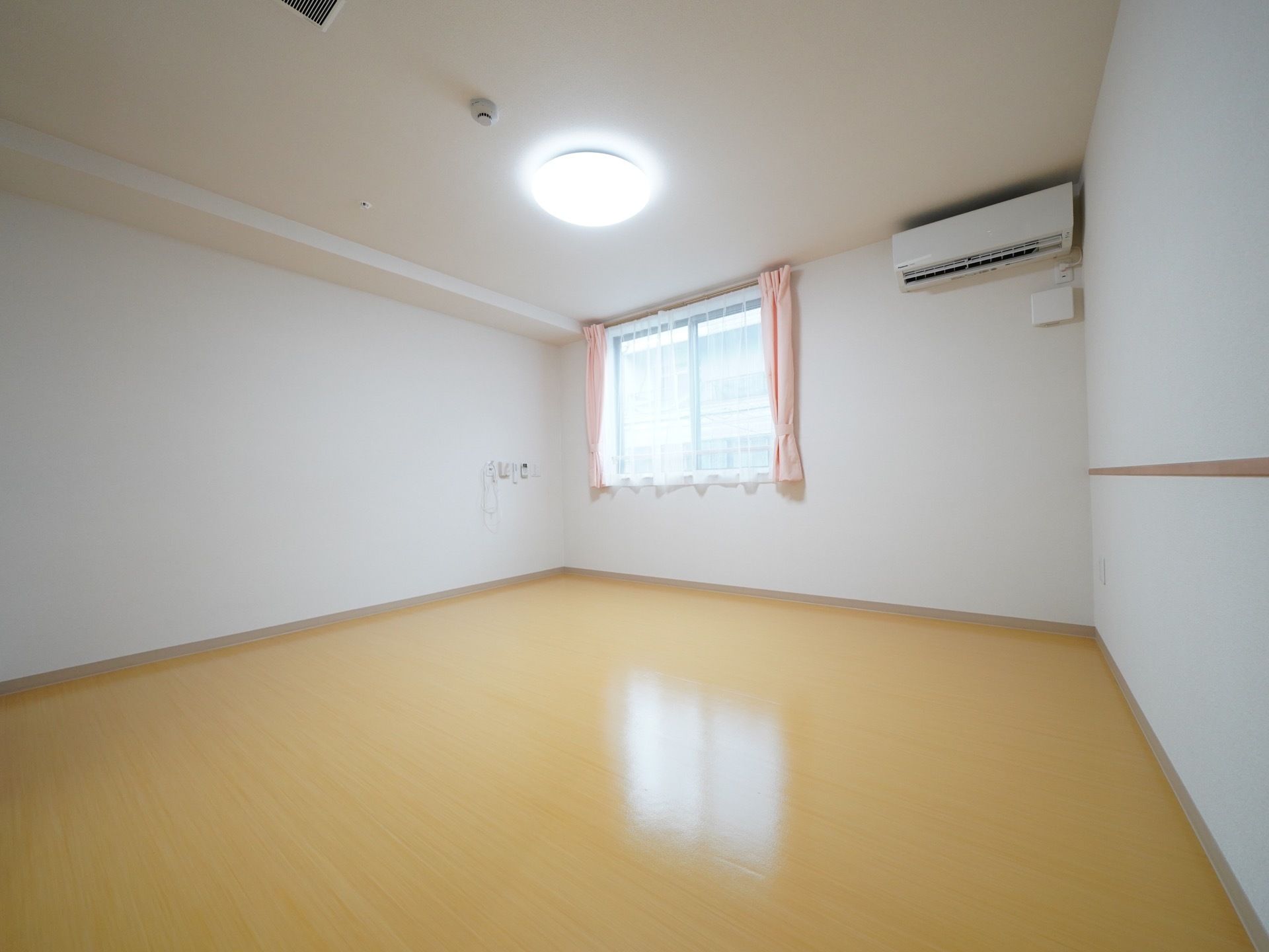 窓から日差しの差し込む明るい部屋である。窓にはピンクのカーテンが取りつけられている。壁にエアコンが設置してある。