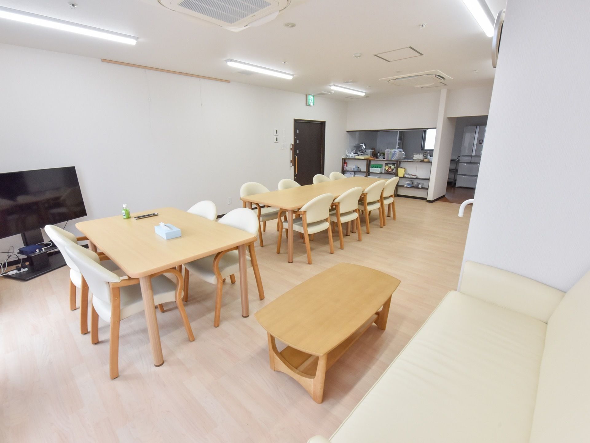 ナチュラルカラーの木のテーブルに、背当てと座面が白色の椅子がセットされている。手前にはソファとコーヒーテーブルも置かれている。