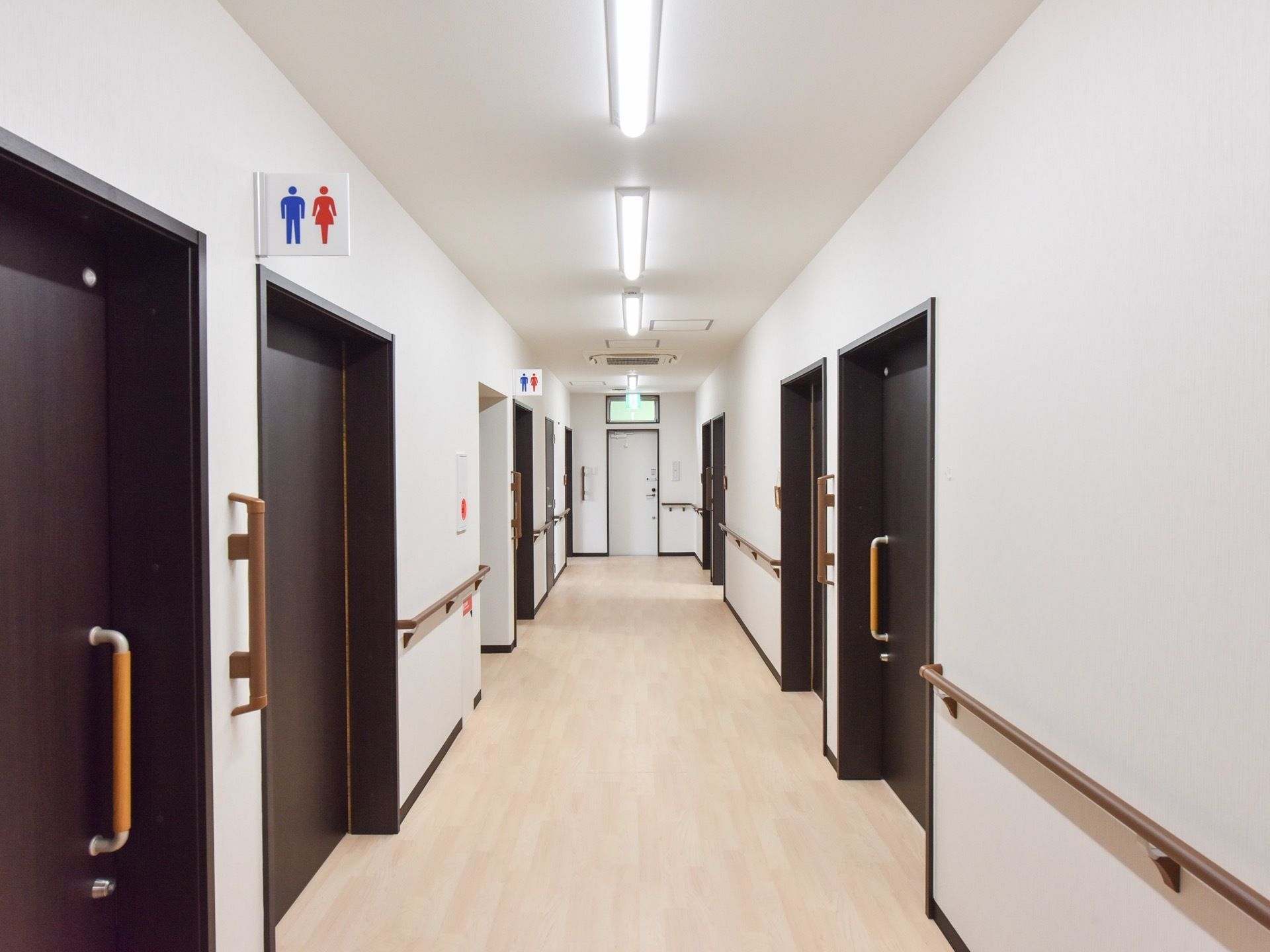 廊下の突き当たりに非常口の扉がある。廊下の左側に共用のトイレが二つあり。右側に居室のドアが並んでいる。