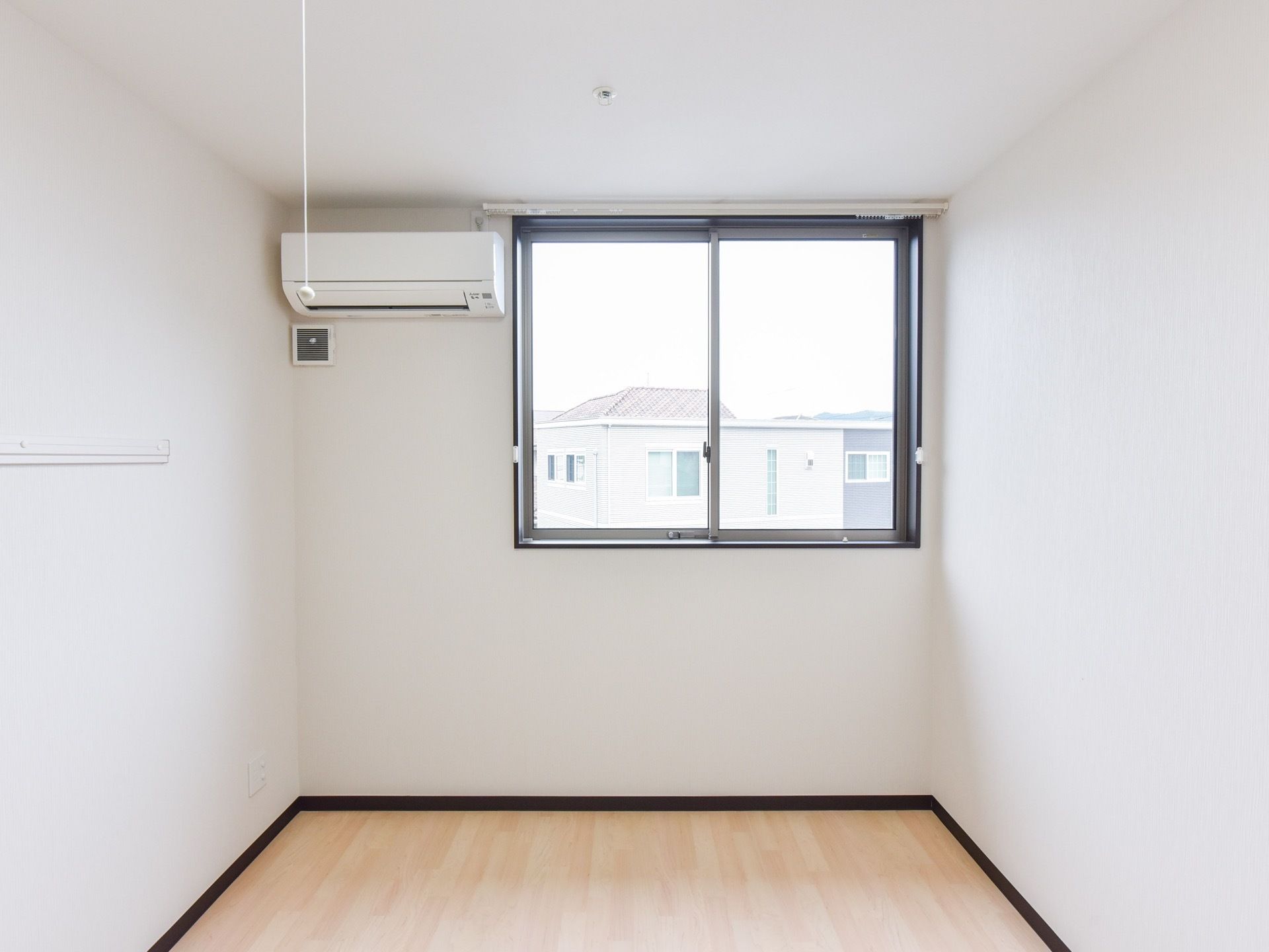白を基調とした内装の居室である。壁にはエアコンとコンセントが設置されており、窓からは外の景色が良く見える。
