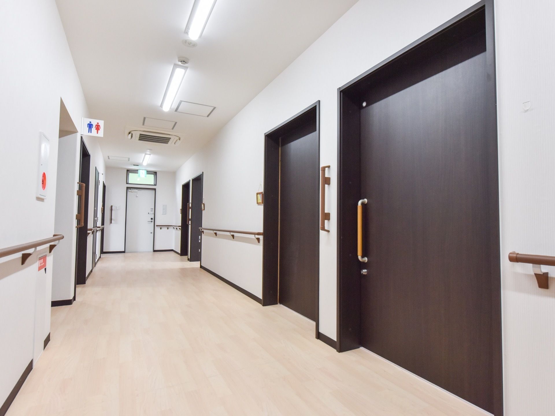 白い壁に手すりや非常ベルが設置されたトイレ前の廊下