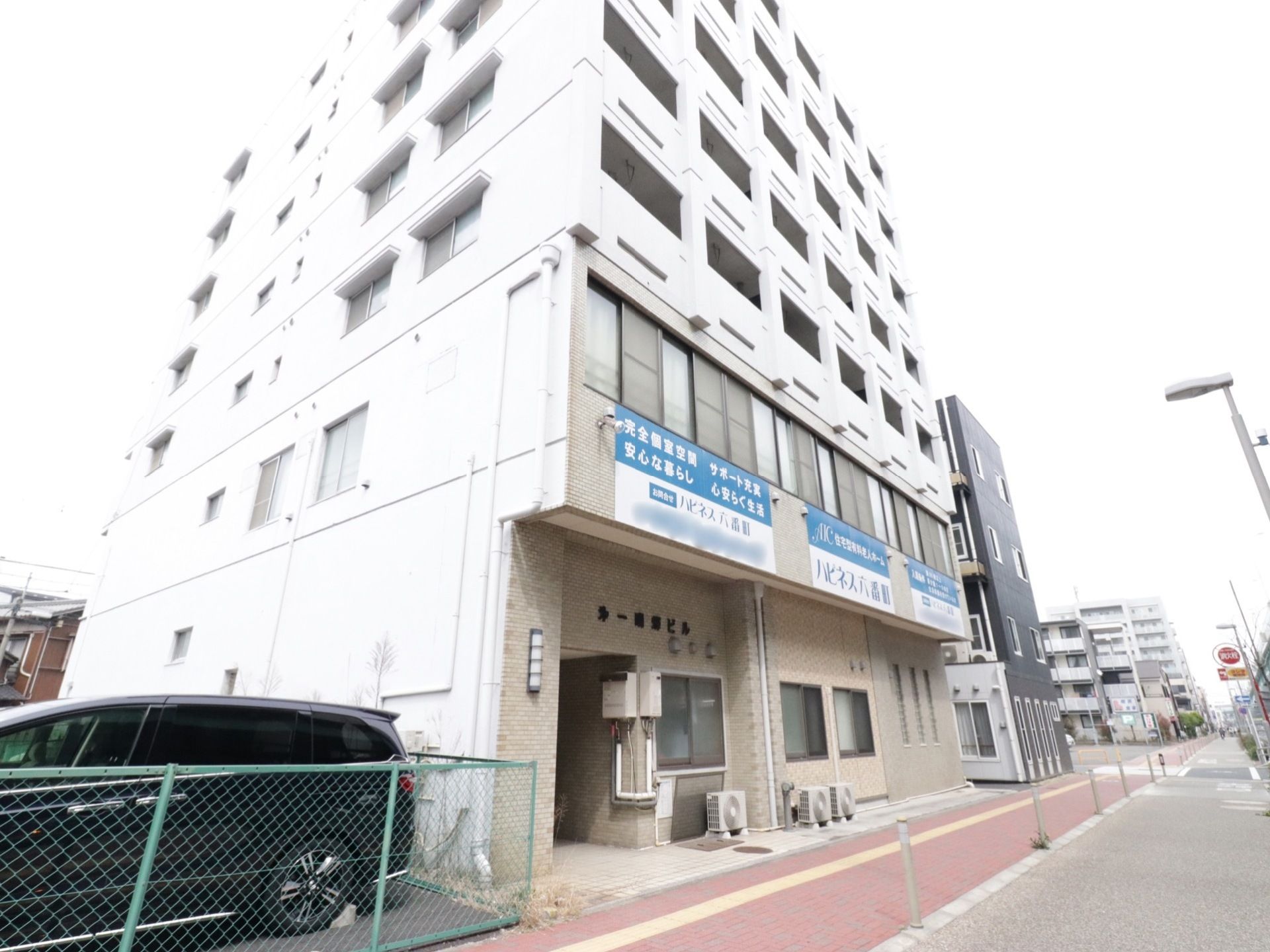 ベランダのあるコンクリート調の建物が建っている。前には歩道があり、レンガが貼られるなどして舗装されている。
