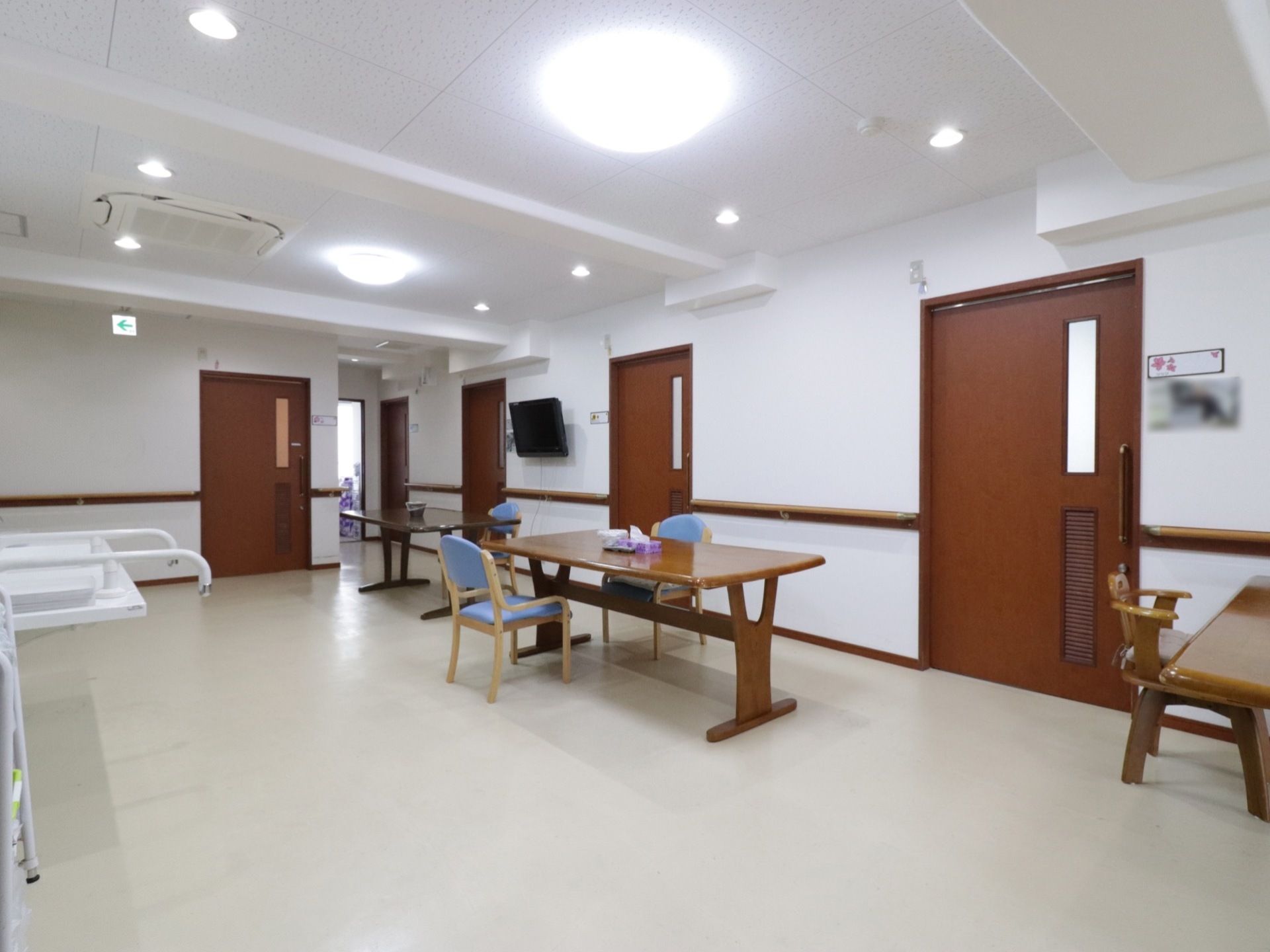 白い壁に木目調のドアが際立って見える。椅子やテーブルの置かれている空間である。壁に手すりが設けられている。
