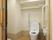 個室トイレの入り口は取っ手のついたスライド式の扉になっている。洋式便座の上に物を置く棚がかかっている。