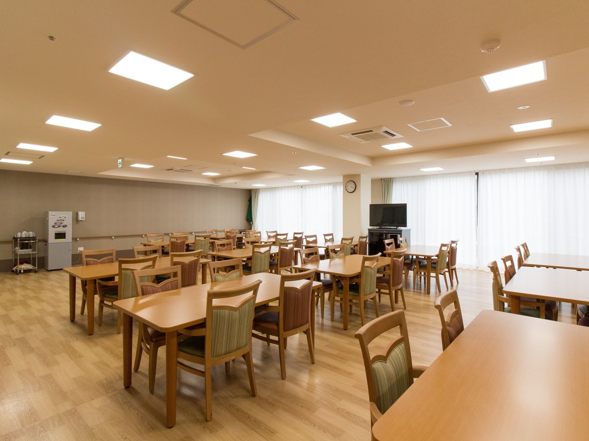 食堂に多くの椅子やテーブルが置かれている。壁際には給茶機があり、その横にコップがたくさん積まれている。
