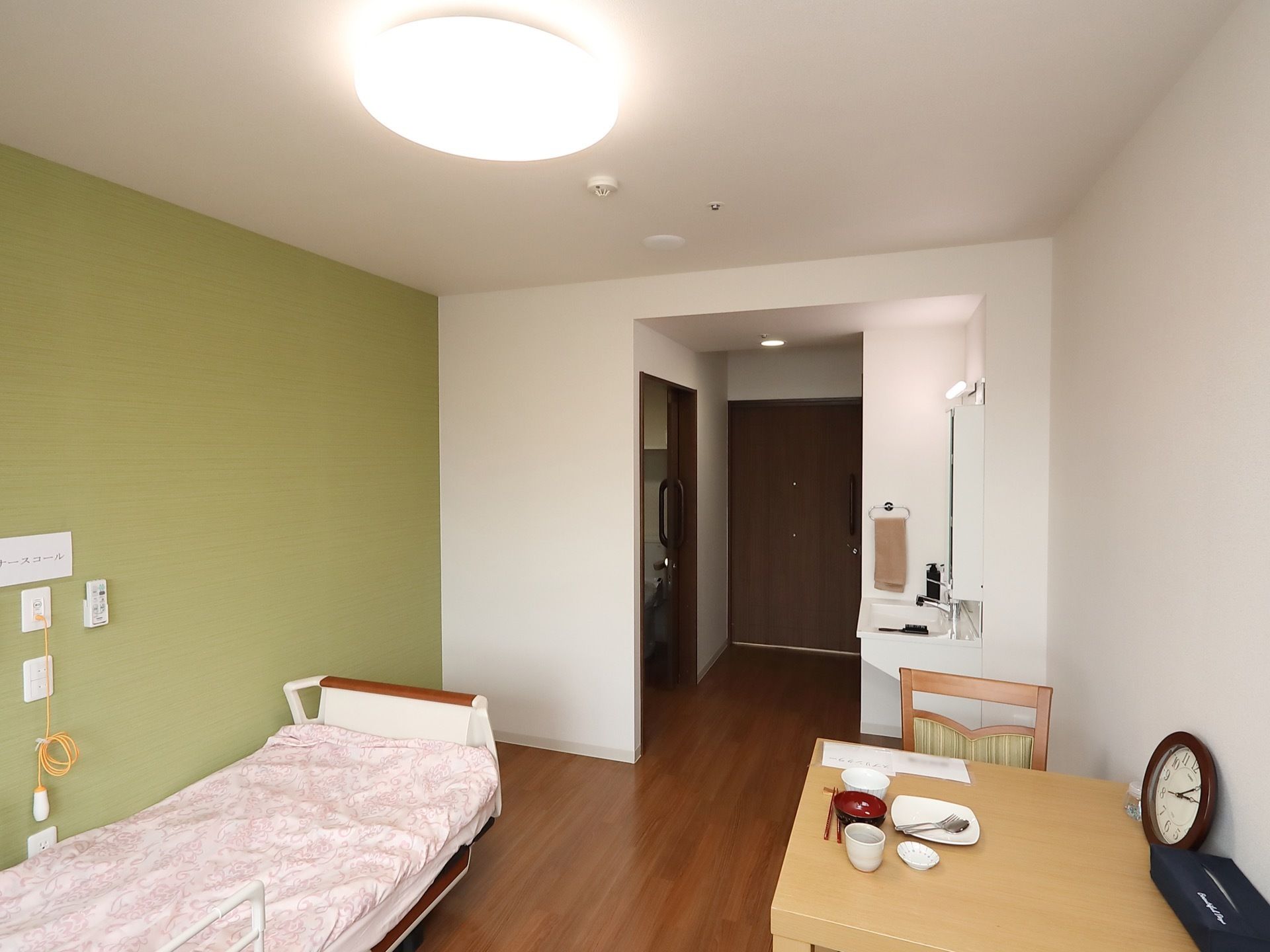 出入口付近に比べると、部屋の部分は幅が広くなっていて、ベッドやテーブルが置かれている。出入口の近くに、トイレスペースが見える。