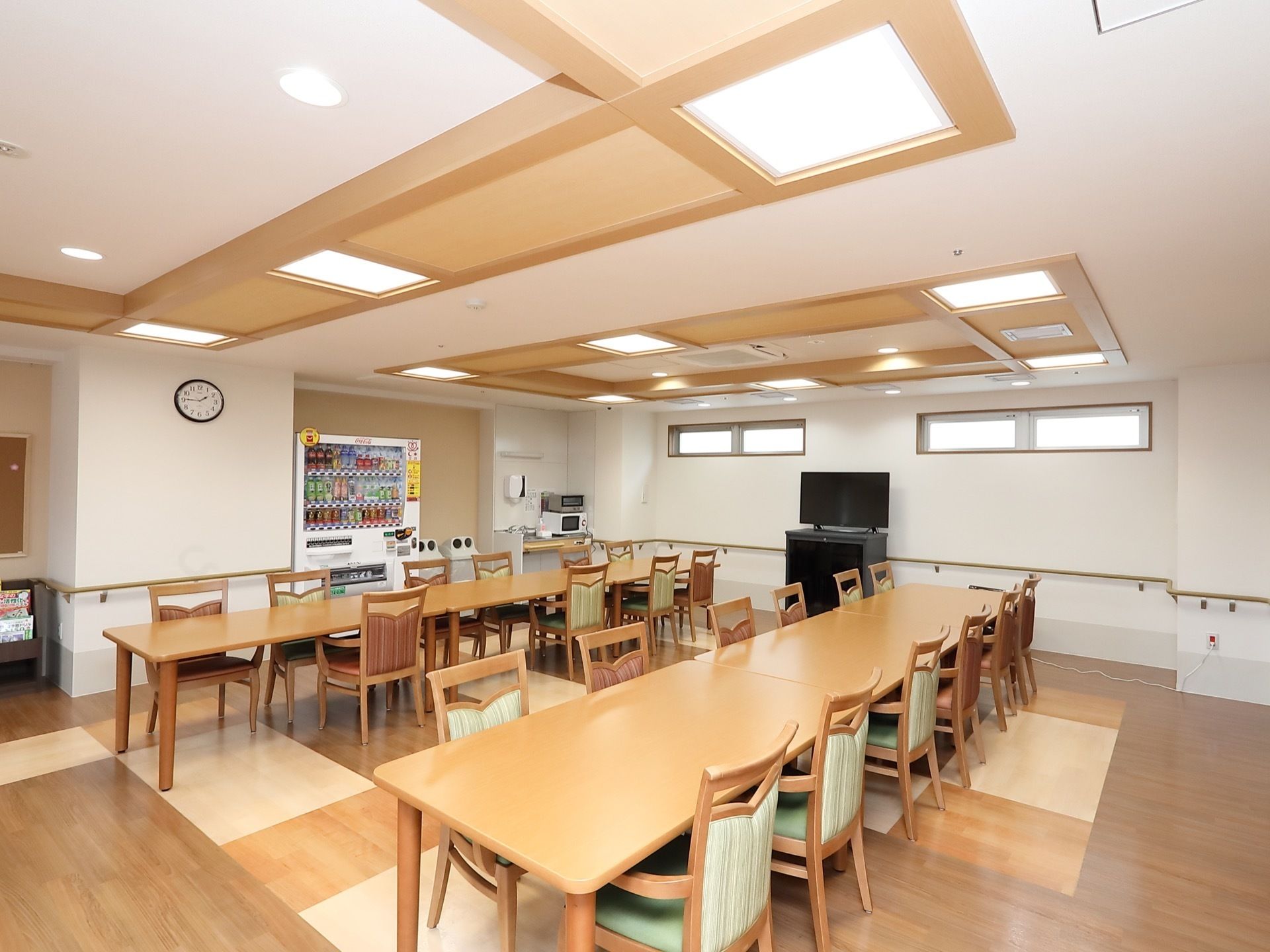 テーブルや椅子が整然と並べられている共用スペースである。飲料の自動販売機や大型液晶テレビが置かれている。