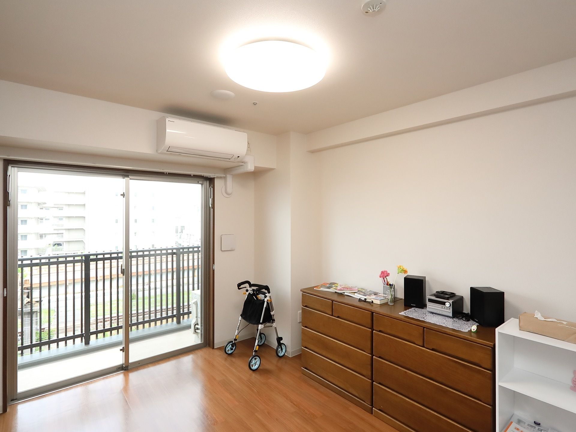 フローリングの部屋に、複数の収納棚が置かれている。天井には丸い大きな照明器具が設置されていて、明るい室内である。