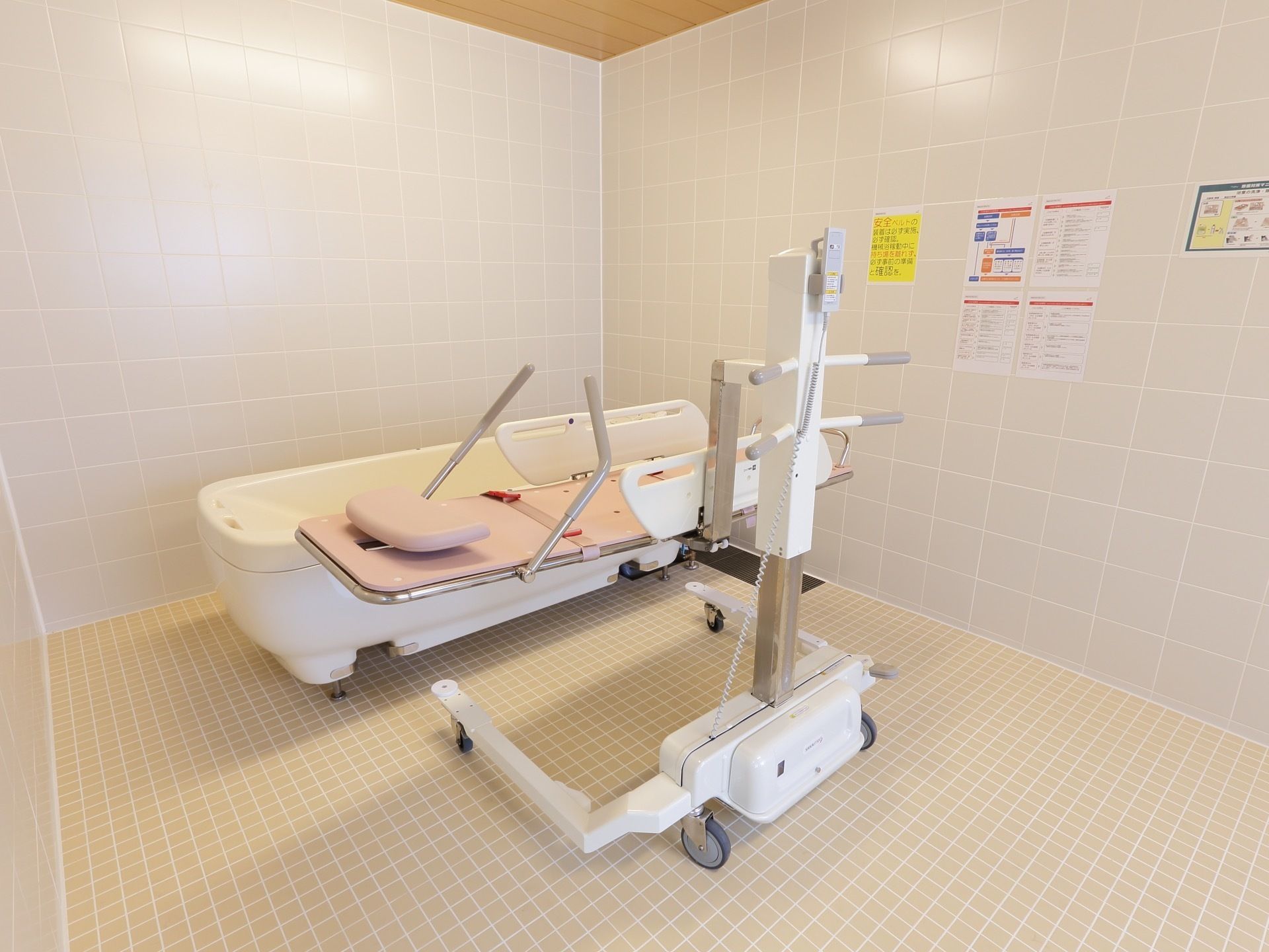 機械浴室はゆったりとした広さがあり、中央には介護用機器が置かれている。壁には、資料が掲示されている。