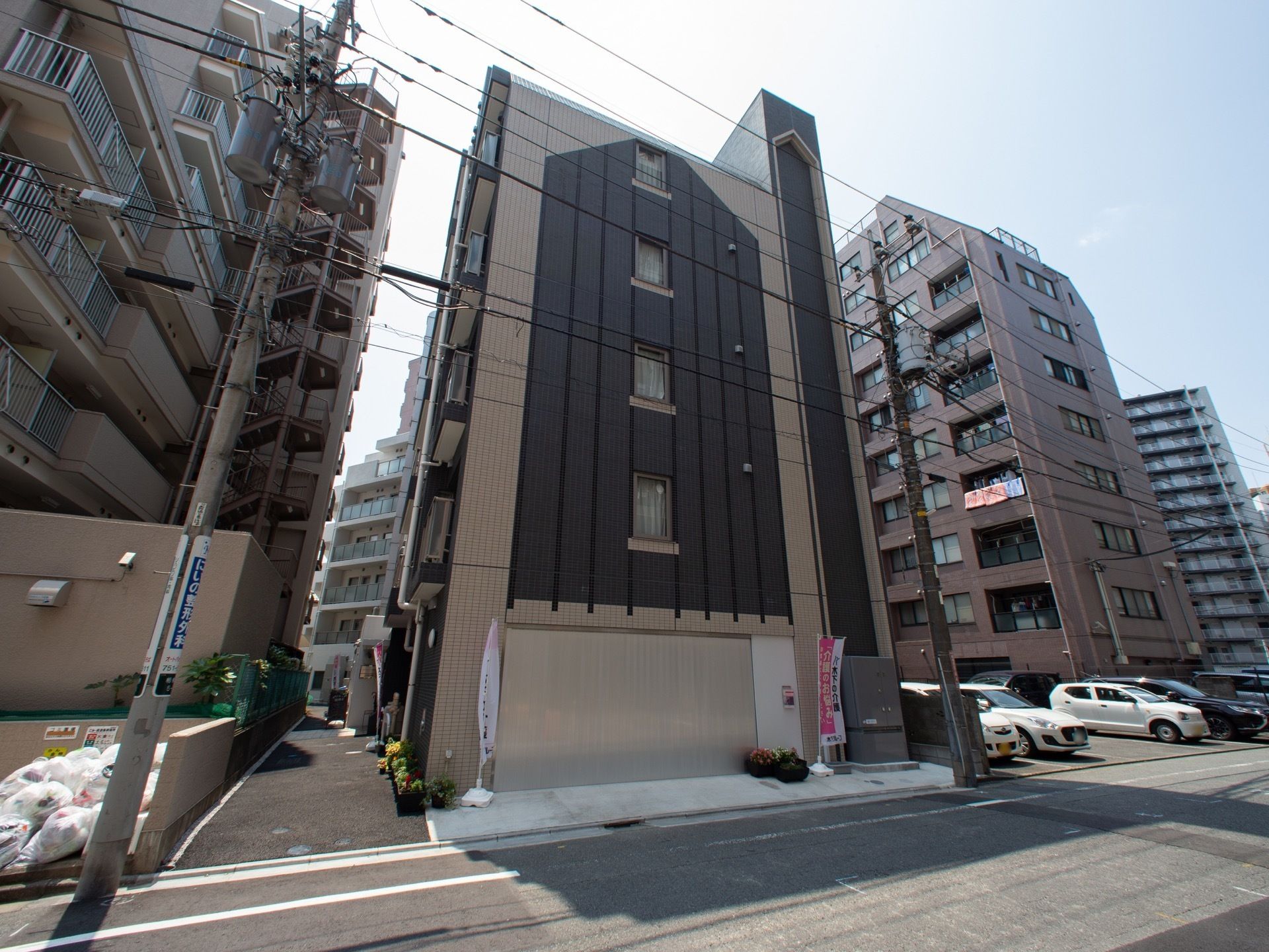 スタイリッシュな外観の６階建ての施設である。左側の壁際には、建物に沿ってプランターが置かれている。周囲には、マンションが建ち並んでいる。