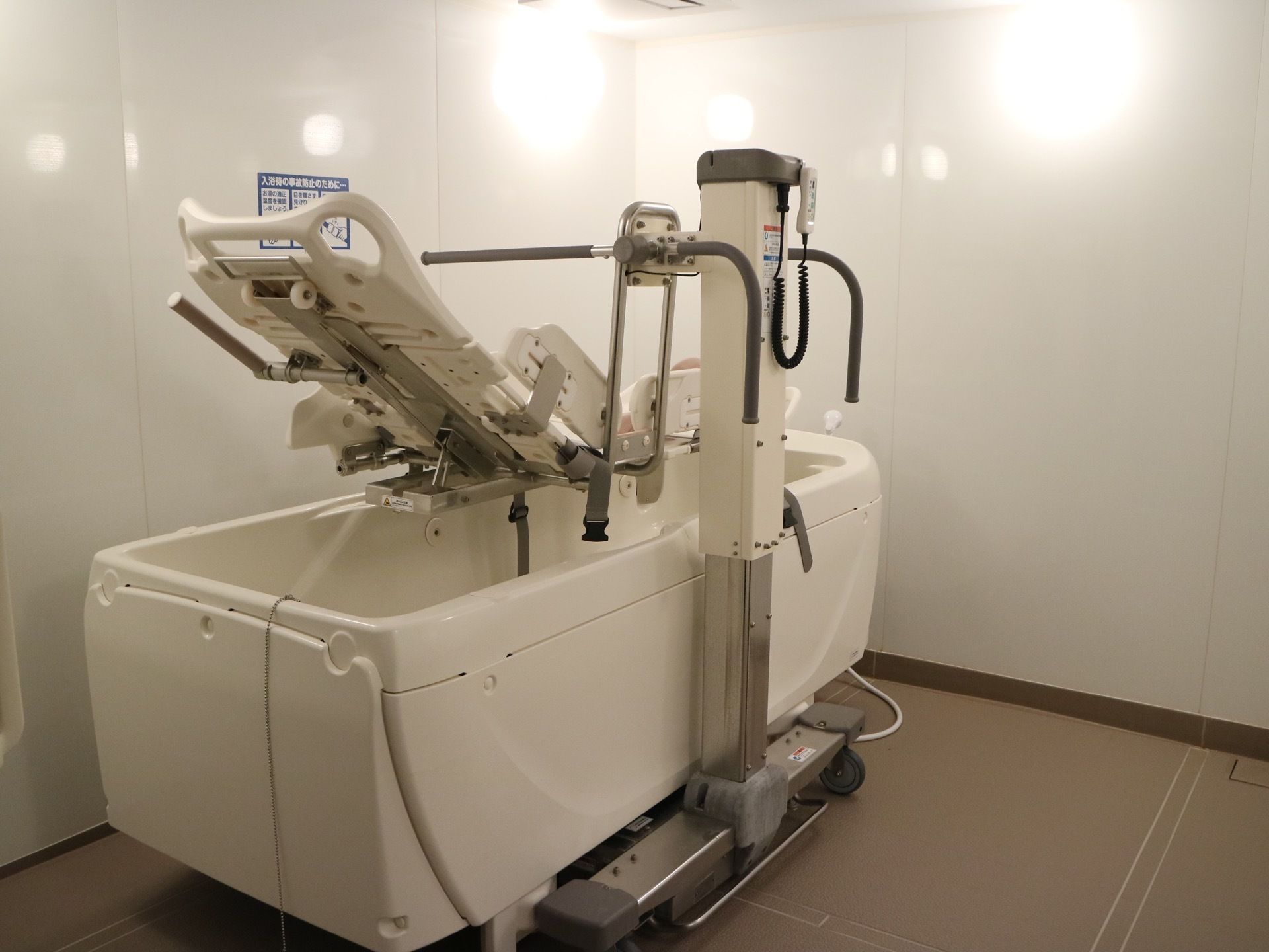 白色の壁にブラウンの床の浴室があり、寝転んだ姿勢で入浴できるタイプの介護用の浴槽がある。