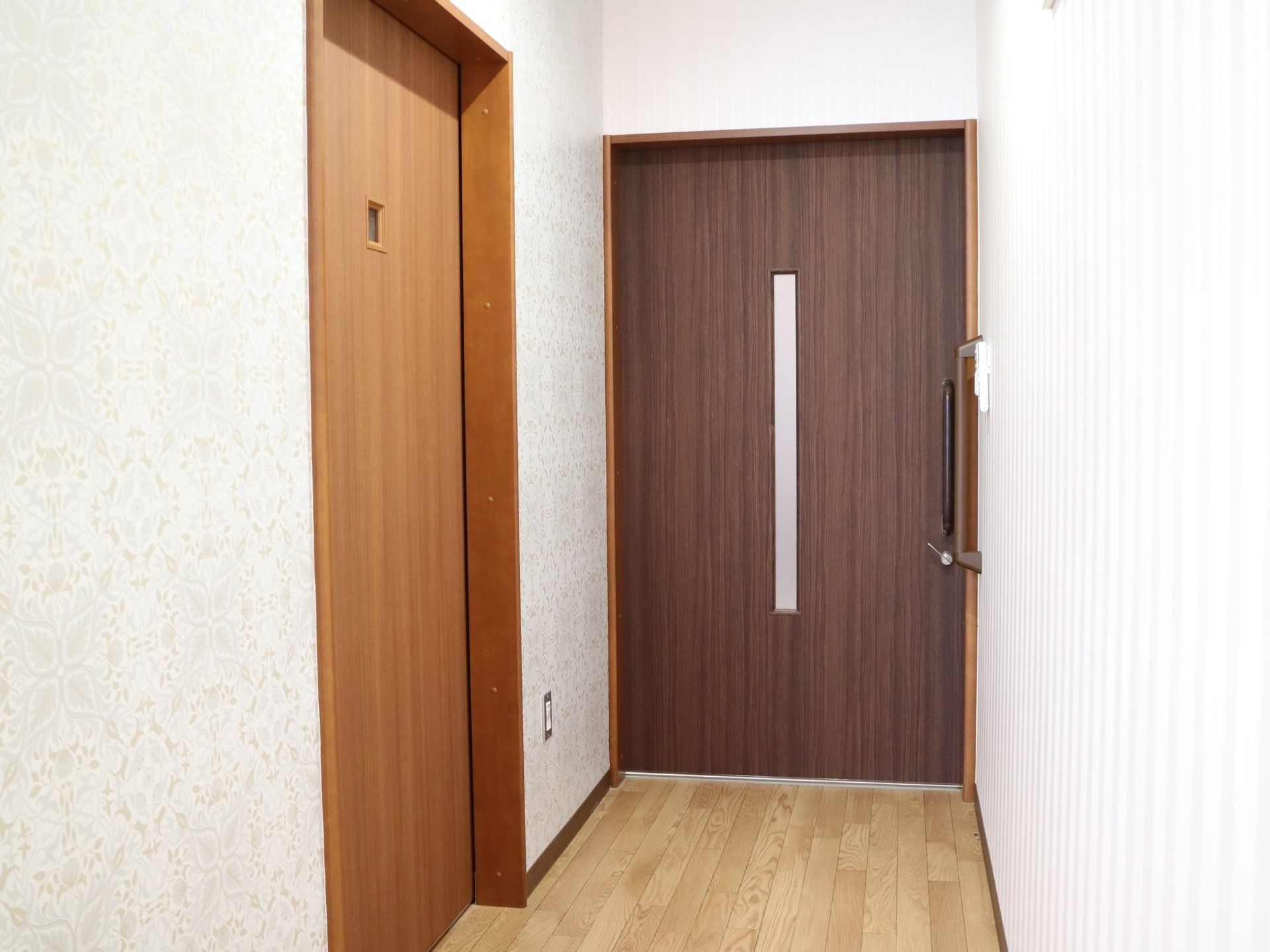 左にトイレの扉があり、正面に居室の入口の扉がある。どちらの扉も引き戸となっていて、入口の隣には縦型の手すりがある。