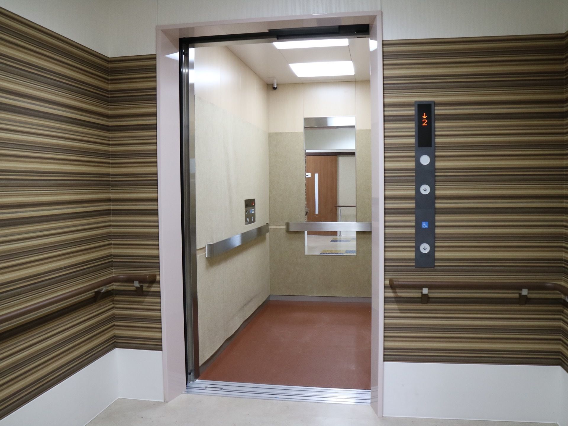 エレベーターが１基正面にあり、エレベーターの内部と周囲の通路の壁に手すりが設置されているのが見える。