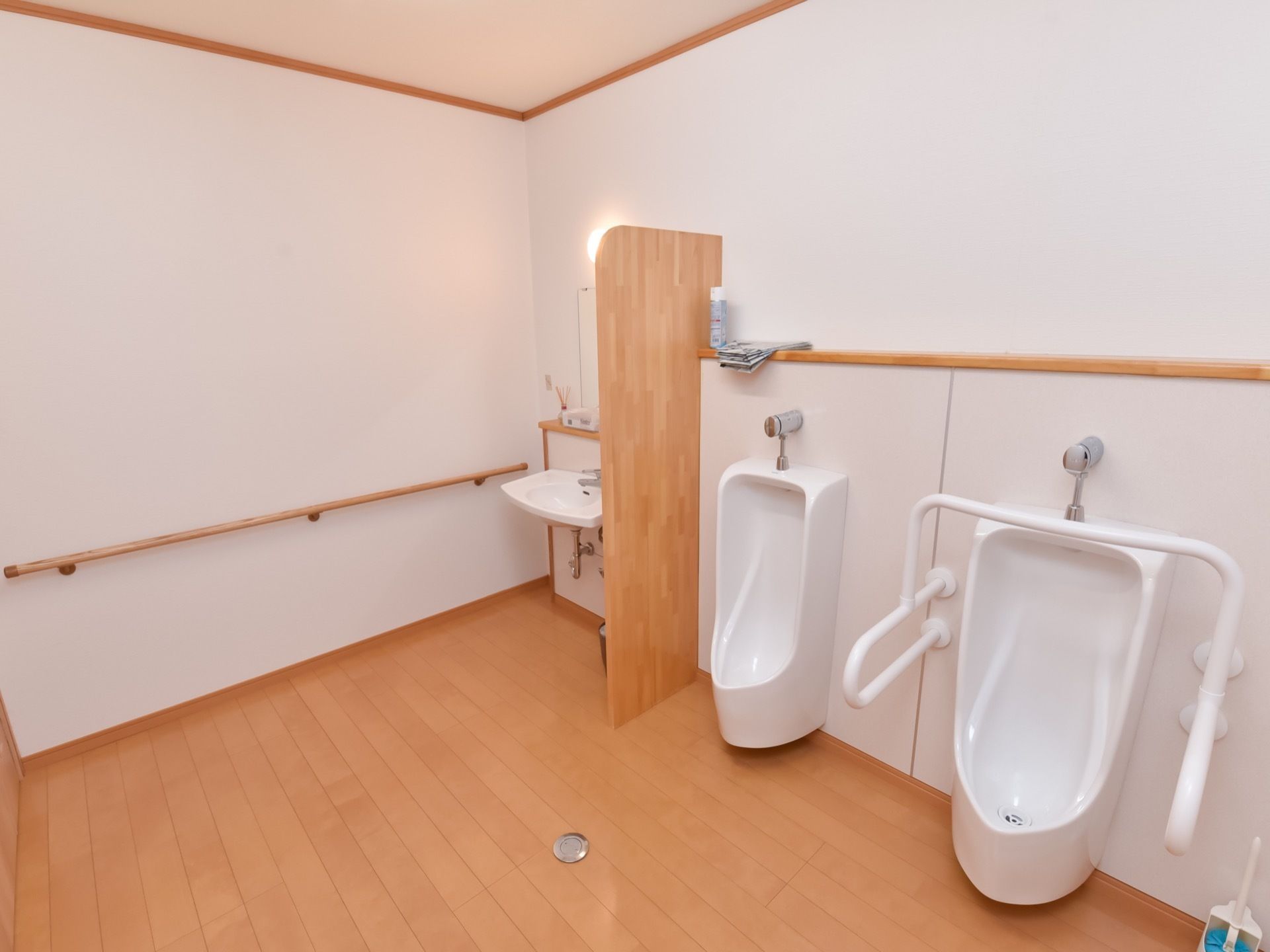 フローリング敷の広々とした男子用トイレには小便器が２台設置されている。壁には手すりが取り付けられている。