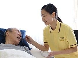 横たわった男性の入居者様に食事の介助をする女性スタッフ