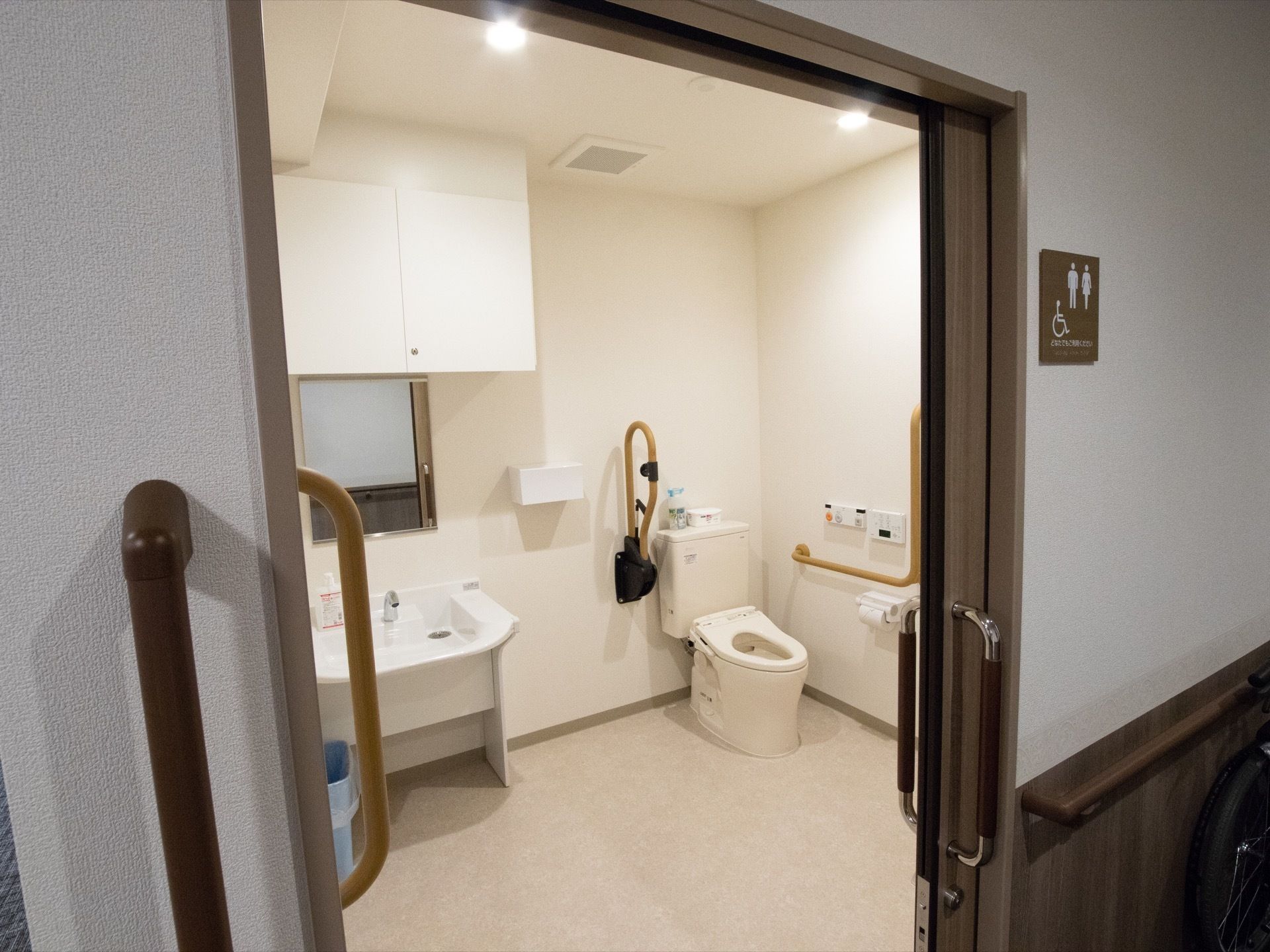 広々とした男女兼用トイレがある。可動式のひじ掛けと手すりが設置されており、トイレの入り口の壁にも手すりがある。