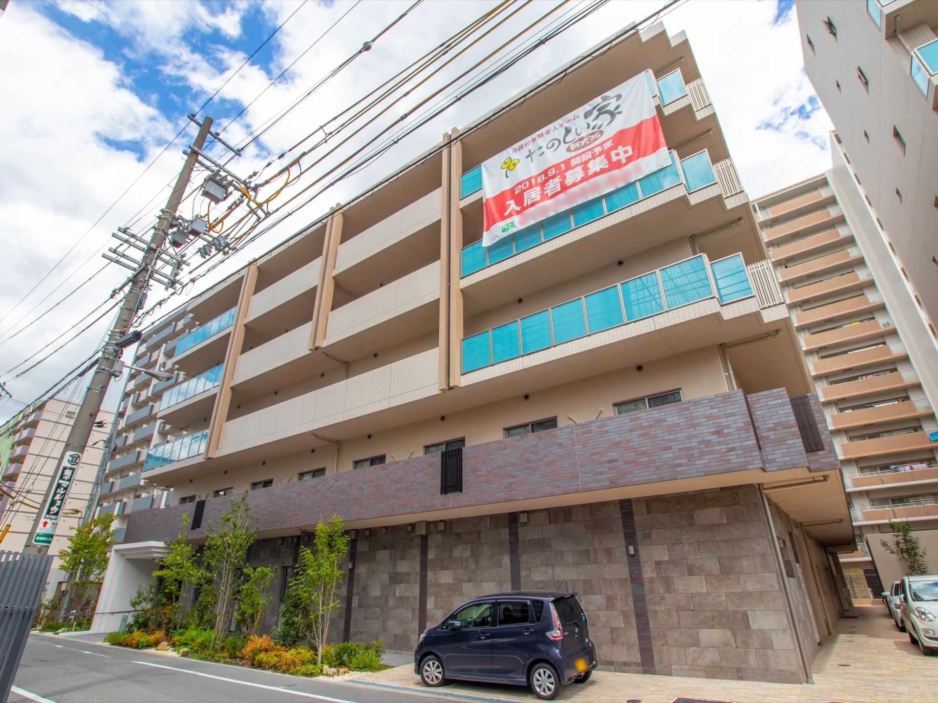 道路沿いに面した五階建ての大きな建物がある。部屋にはベランダがあり、施設の玄関前には駐車スペースがある。