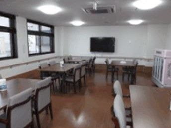 壁際にはぐるりと手すりが設置されている食堂。４人掛けのダークブラウンのテーブルが並ぶ。壁には大型のテレビがある。
