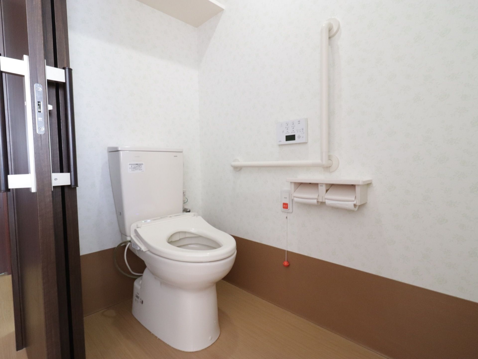トイレの入り口は大きな引き戸になっている。内部は白を基調にしていて清潔感がある。便座にはフタがなく、壁に手すりが付いている。