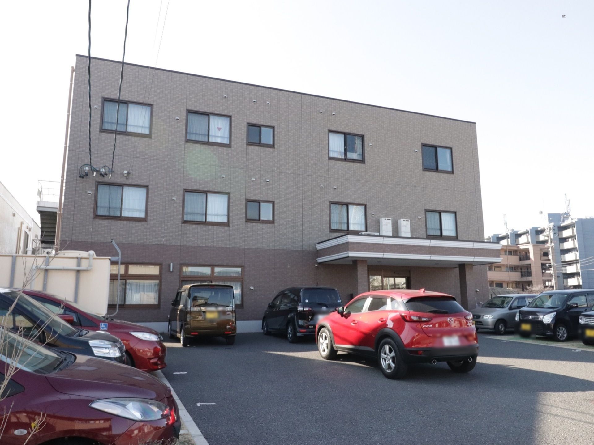 ３階建ての施設前面に設けられた駐車場に停車する複数台の乗用車