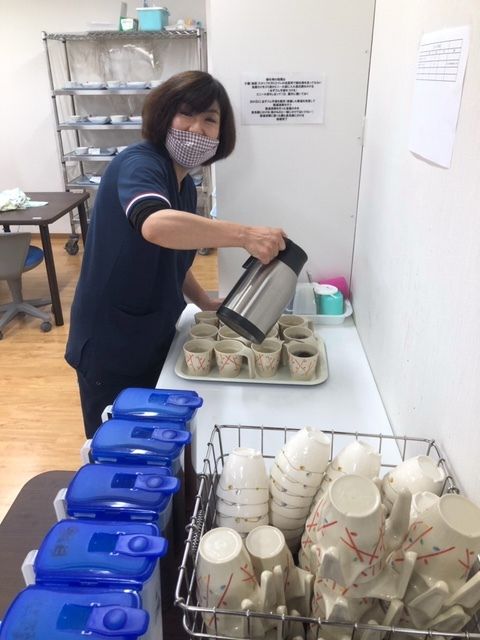 手前には洗われた湯呑とお茶のポットが並び、奥ではマスクをしたスタッフが入居者のお茶を用意している。