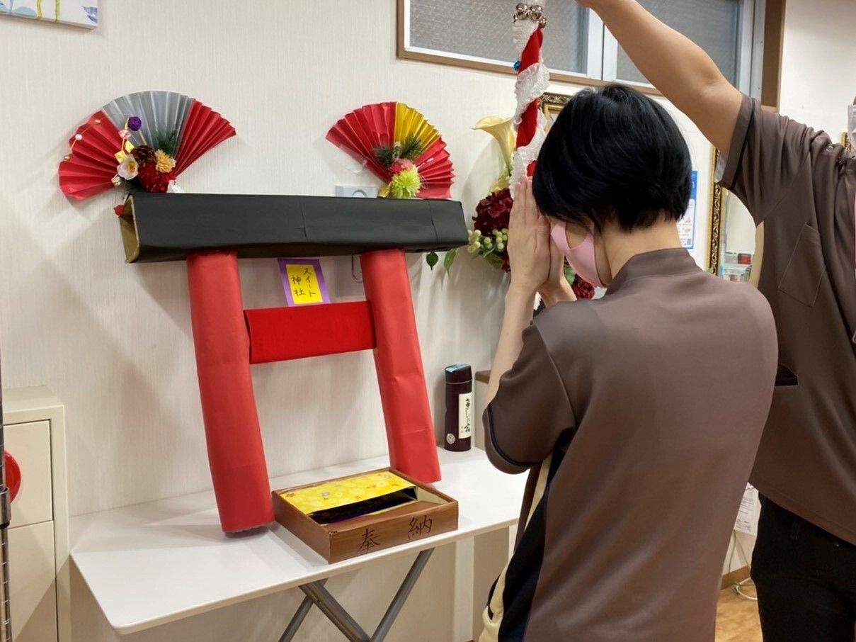 壁際に手作りの神社の鳥居を立て掛け、その前で拝む女性スタッフ