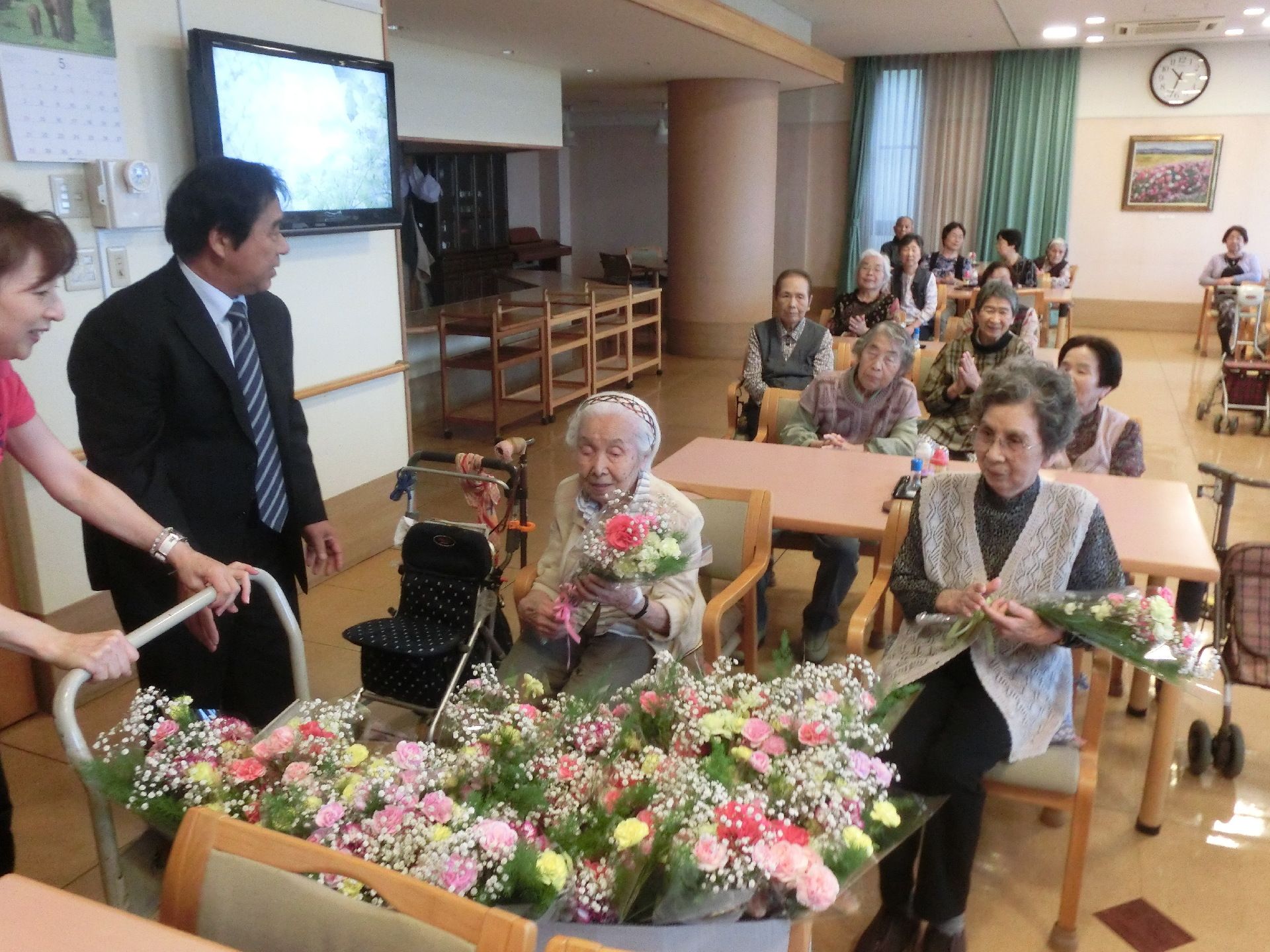 椅子に腰かける入居者様皆さまにスタッフが花束を配っている光景