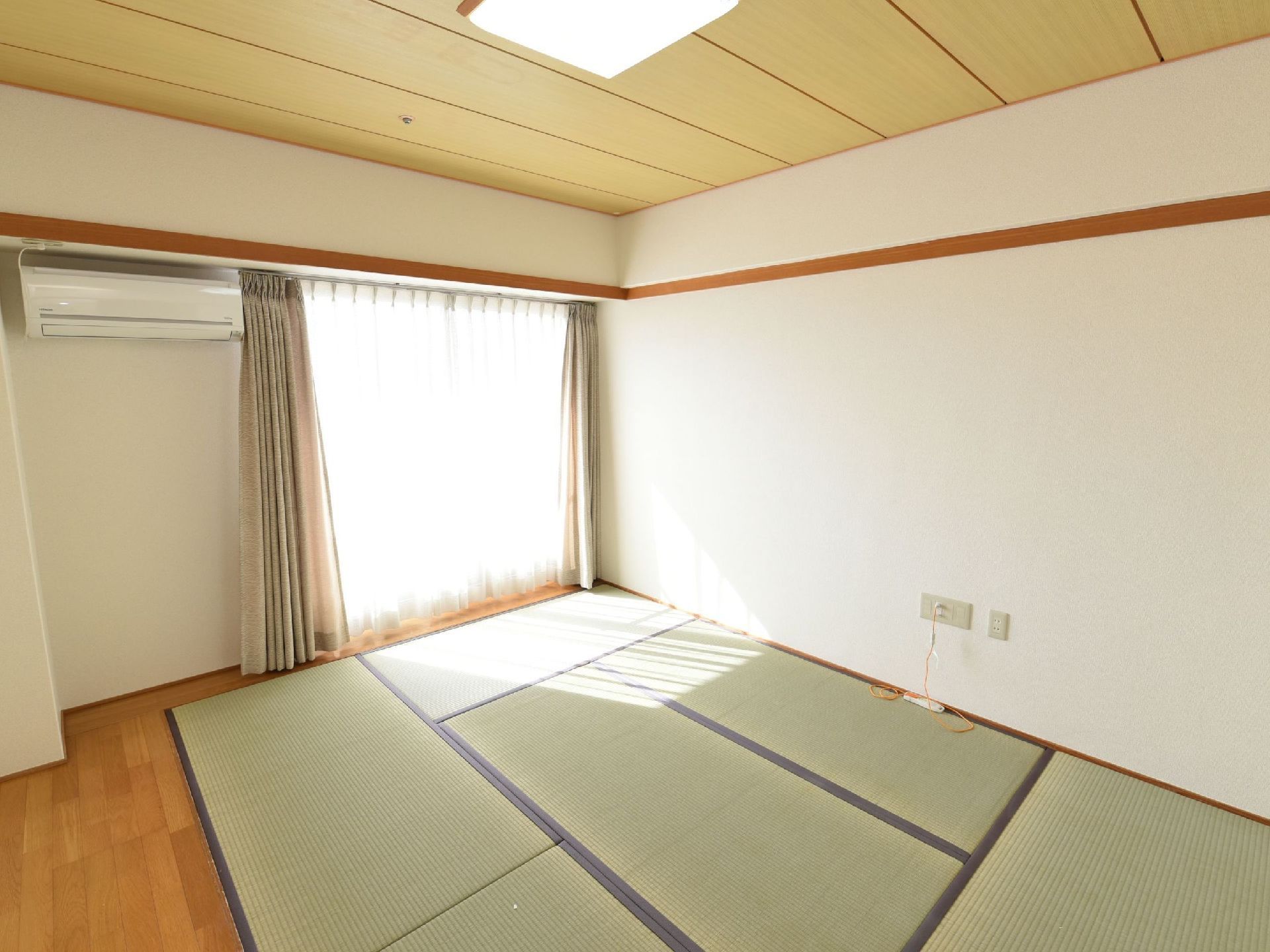 ６畳のたたみの周りがフローリングになっている居室である。大きな掃き出し窓があり、その脇にはエアコンが設置されている。