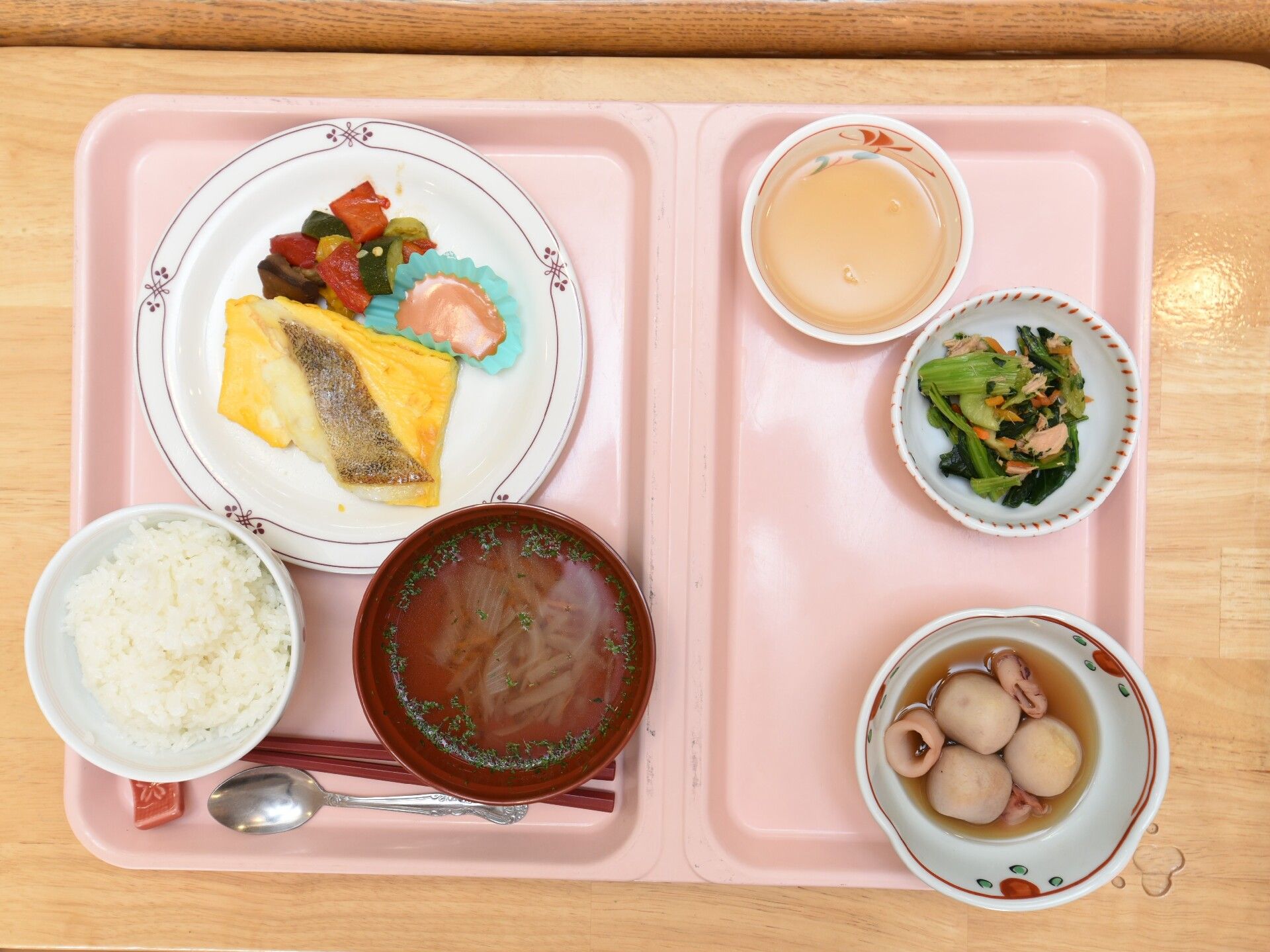 ご飯、みそ汁の他に、おかず３皿とお茶がピンク色のプレートに置かれている。ワゴンに乗せられ、配膳されるとことろである。