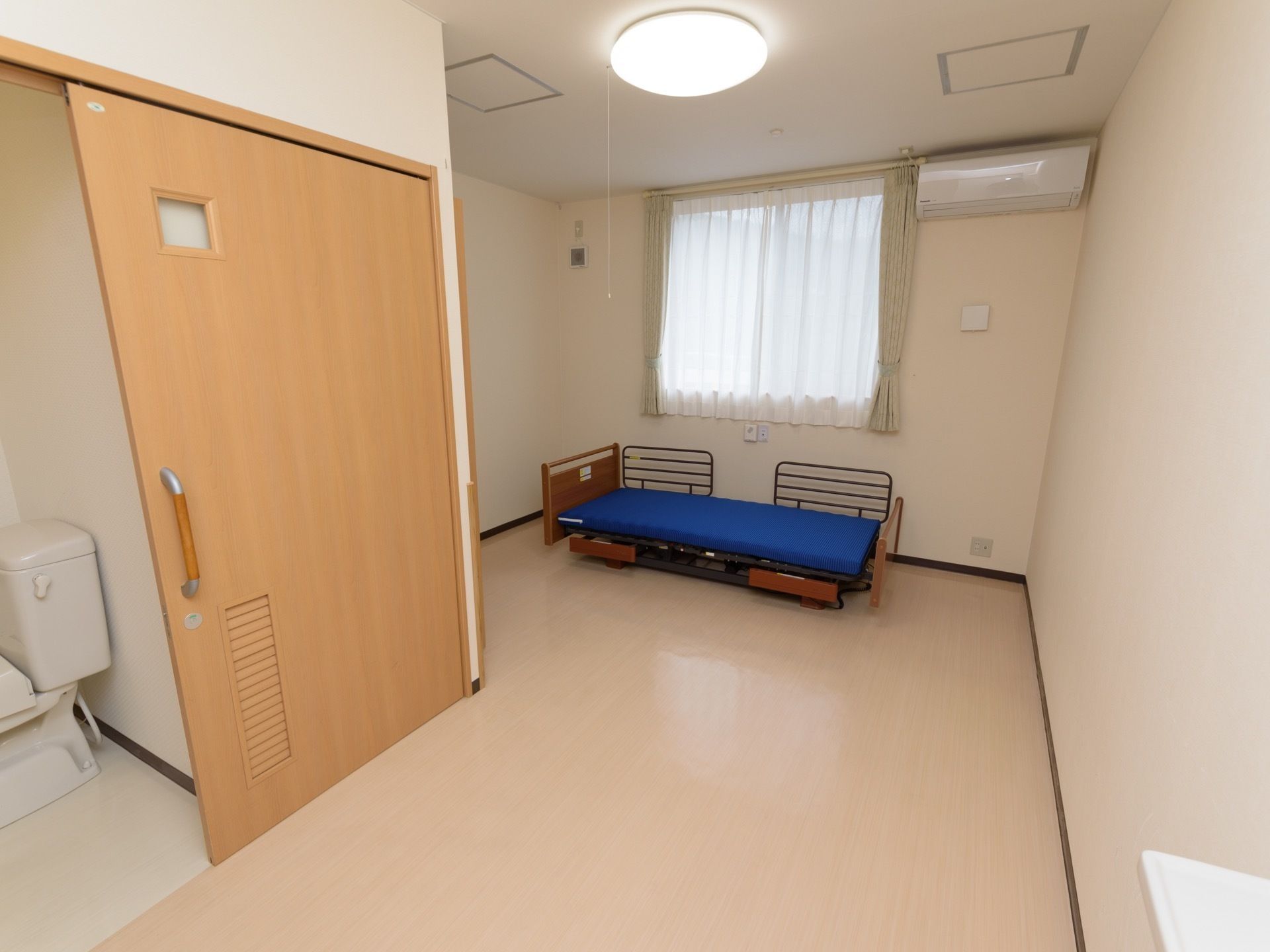 エアコンや介護ベッド、トイレが備わった居室である。広めの間取りになっており、自然光が差し込む窓が設けられている。