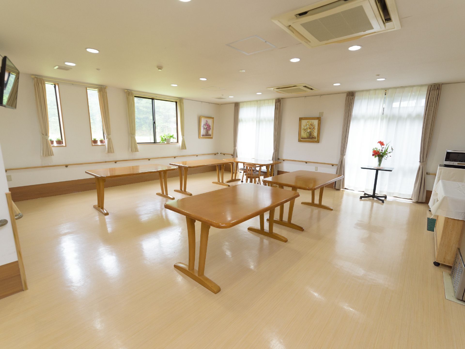 木目調のテーブルが複数台配置され、壁伝いに手すりが設置された共有スペース