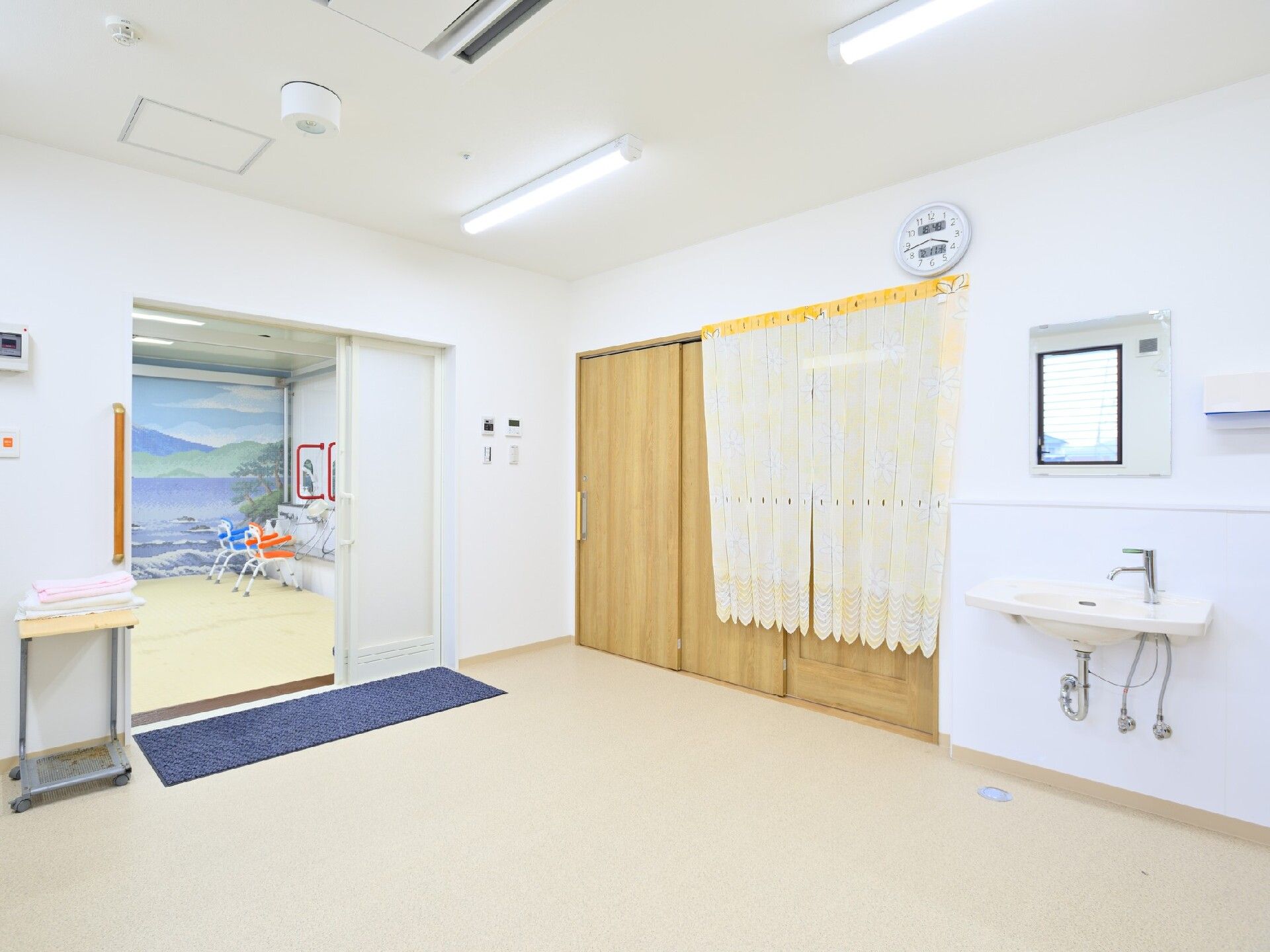 広い脱衣所には手洗い場があり、浴室へ続くドアはワイドタイプで段差がない。浴室内にはシャワーチェアが置かれ、富士山の壁画も見える。
