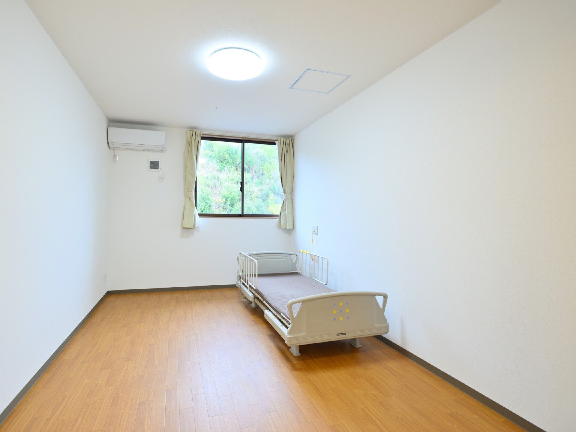 フローリングの部屋はシンプルな造りで、窓と介護用ベッド、エアコンが付いている。ベッドサイドには緊急通報装置もある。