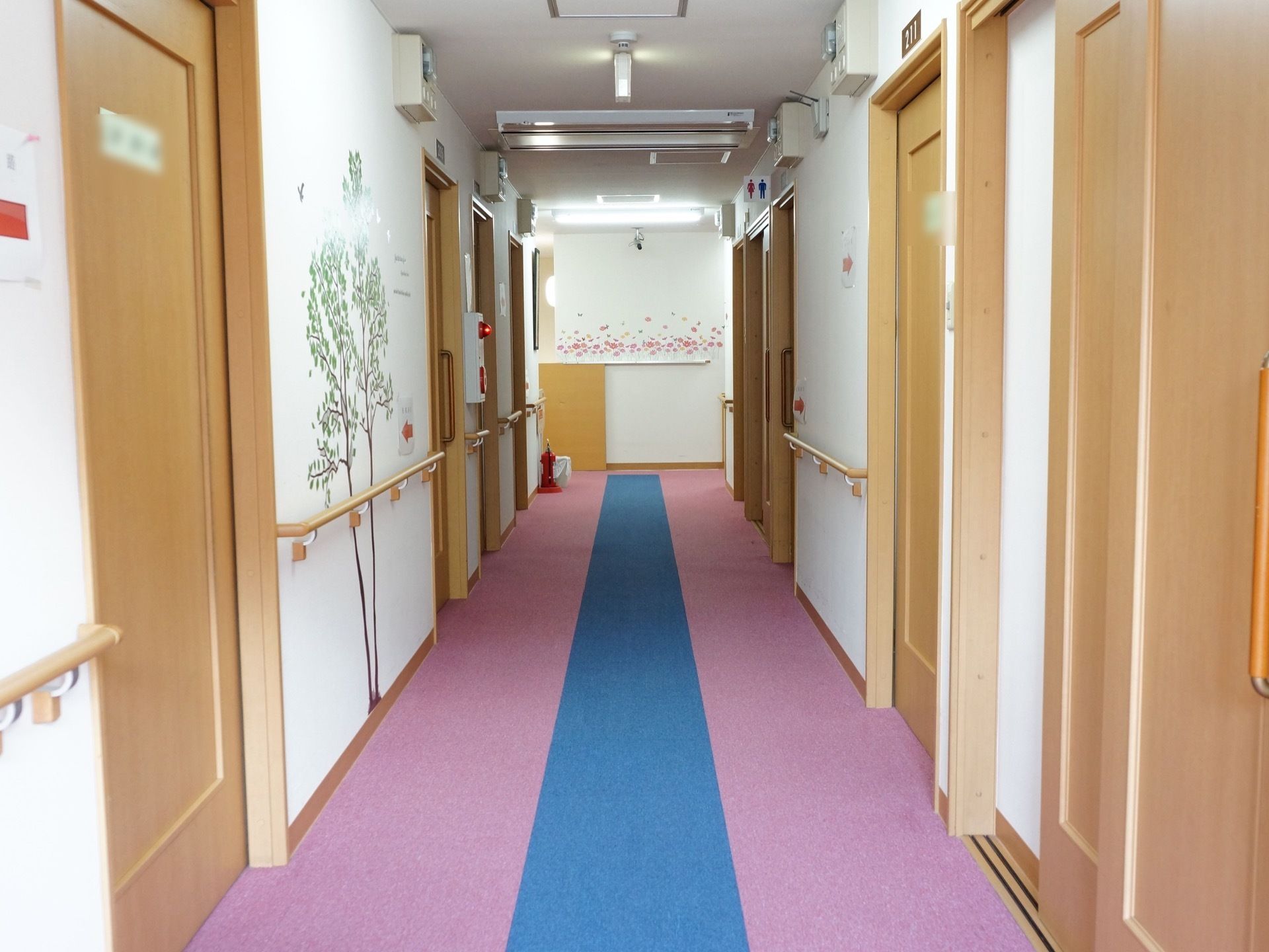 居室のドアは木目調の温かみを感じるものとなっている。壁面は植物のデザインが施されており、入居者様の部屋の目印にもなっている。