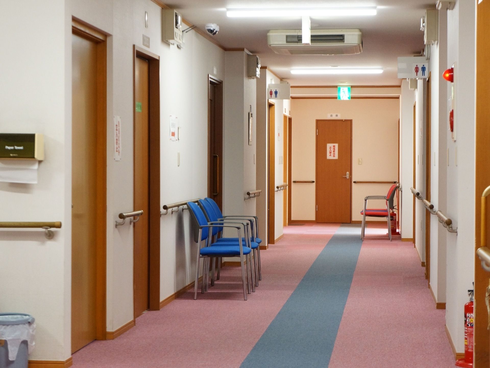 スライド式のドアで仕切られたトイレが両サイドにある。通路の途中には、ひじ掛け付きの椅子が複数置かれている。
