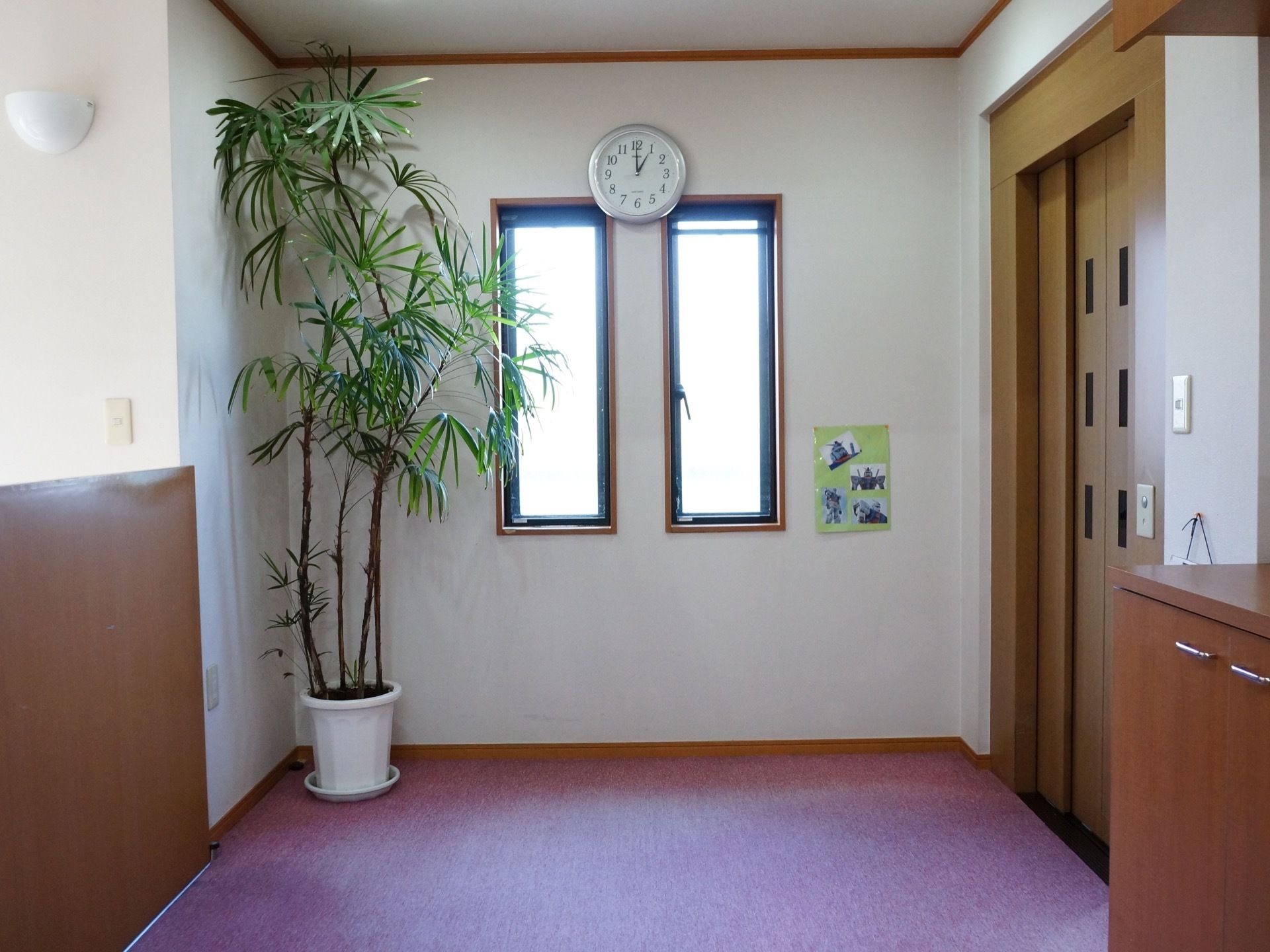 エレベーター前の通路には２つの小さな窓がある。壁には、時計と写真が飾られている。観葉植物が置いてある。
