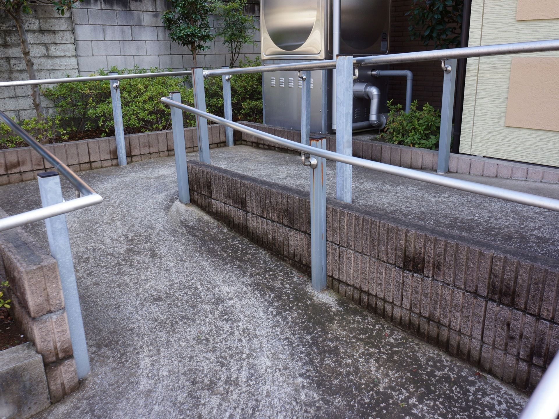 施設前に設置されている緩やかなスロープ。何度か折り返しがあり、両サイドには銀の手すりが設置されている。
