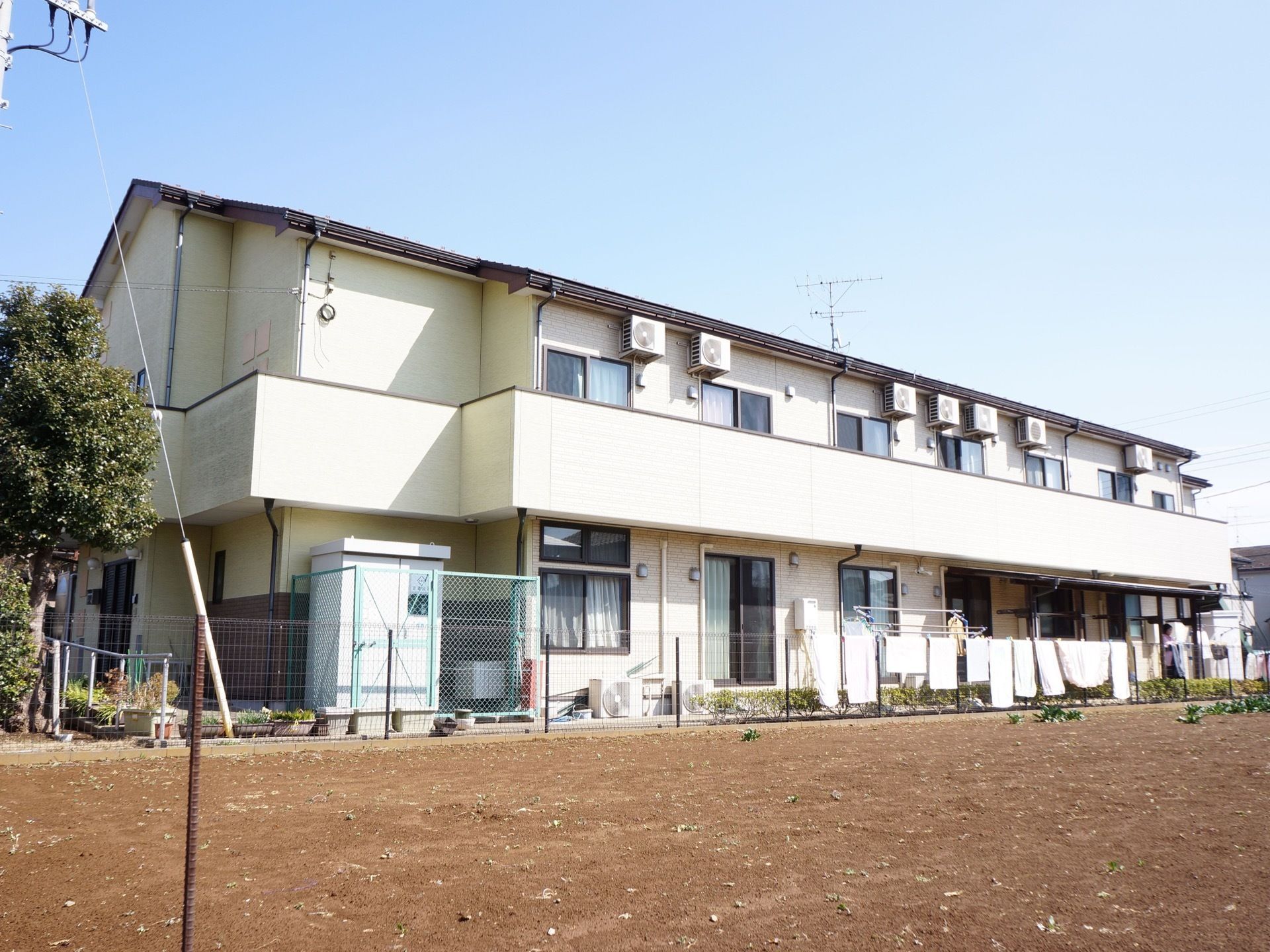 施設の裏側は更地で、何も建物が建っていないので日当たりが良い。柵にはシーツなどが干してある。２階部分にはベランダがある。