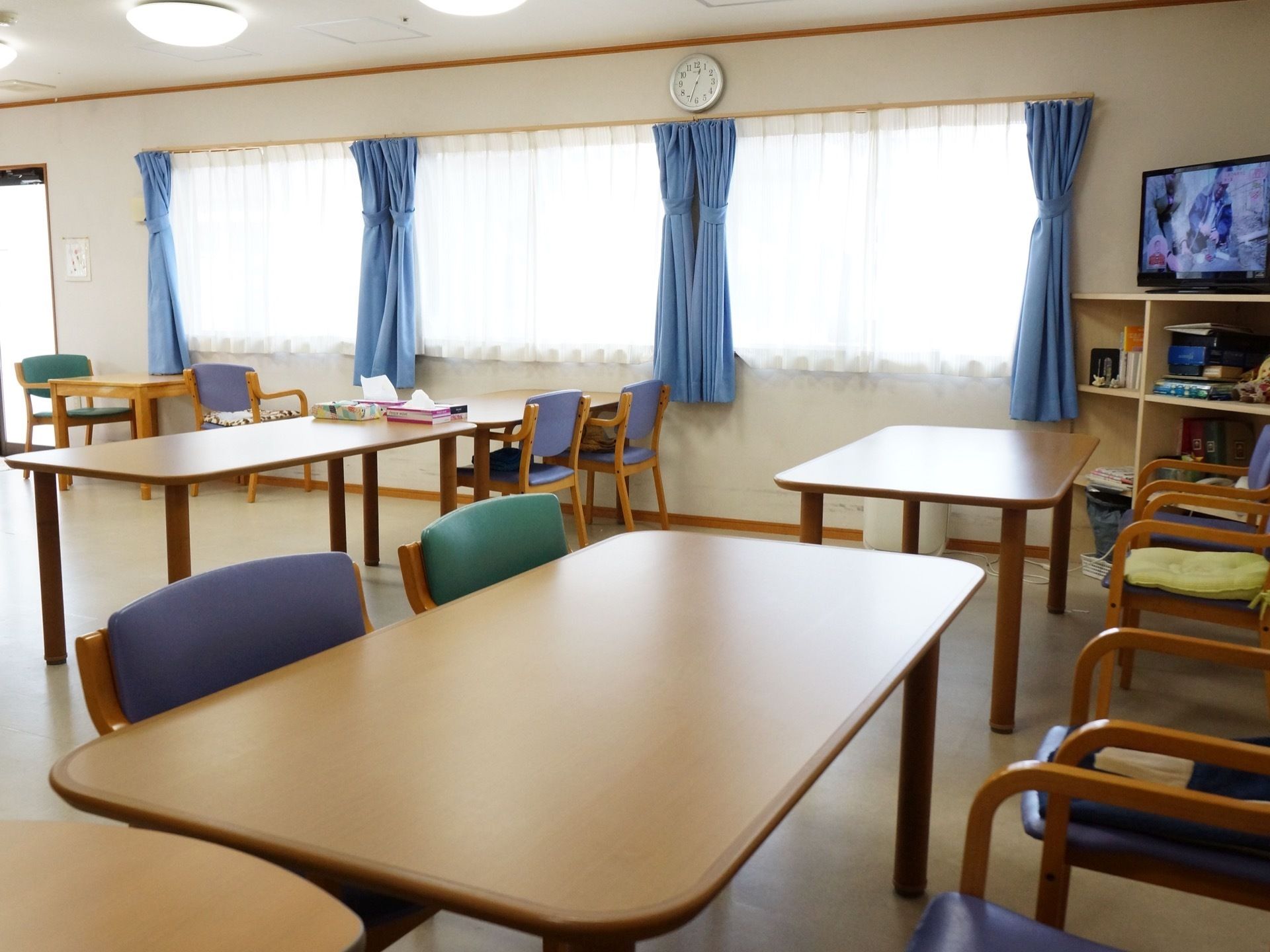 壁一面に大きな窓があり、外へと続くドアが奥にある。室内には、木製のテーブルとひじ掛け付きのテーブルが複数置かれている。