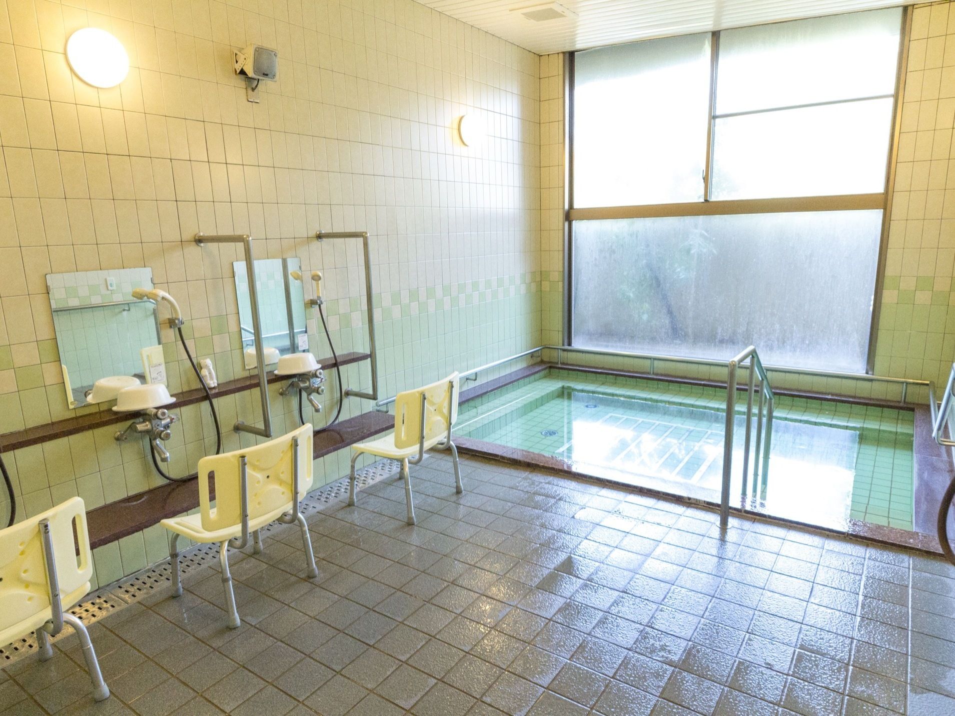 全面タイル貼りの浴室である。洗い場がいくつか設置されていて、シャワーや手すりがある。入浴用介助椅子が置かれている。