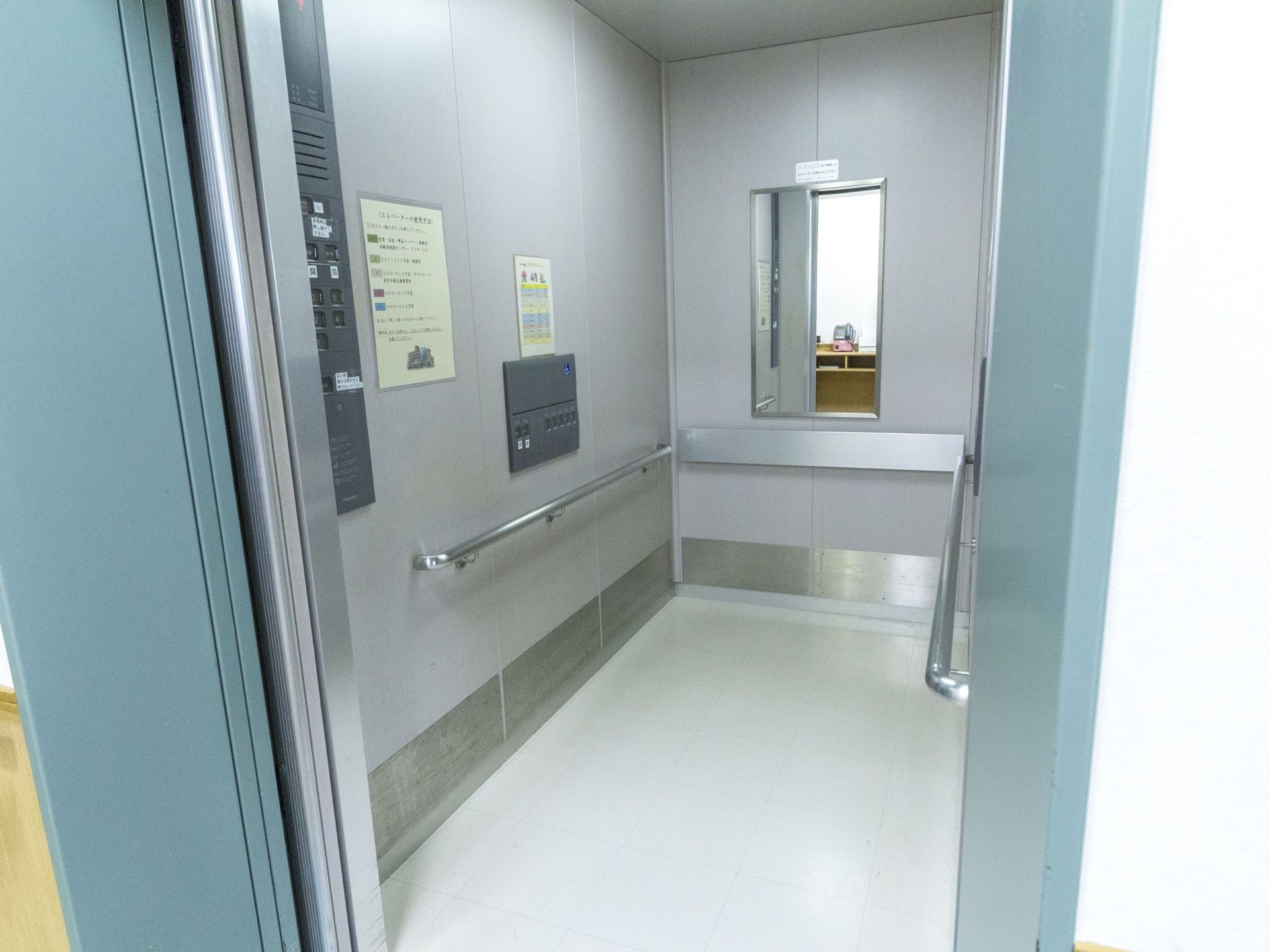 奥行きのあるエレベーターである。壁に手すりが取り付けられていて、昇降ボタンが２か所に設置されている。