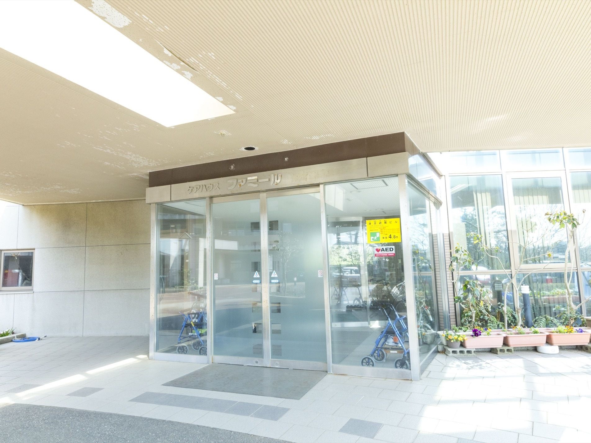 ガラス製の自動ドアが設置されている。入り口前はタイルが貼られていて、きれいに舗装されている。プランターが置かれている。